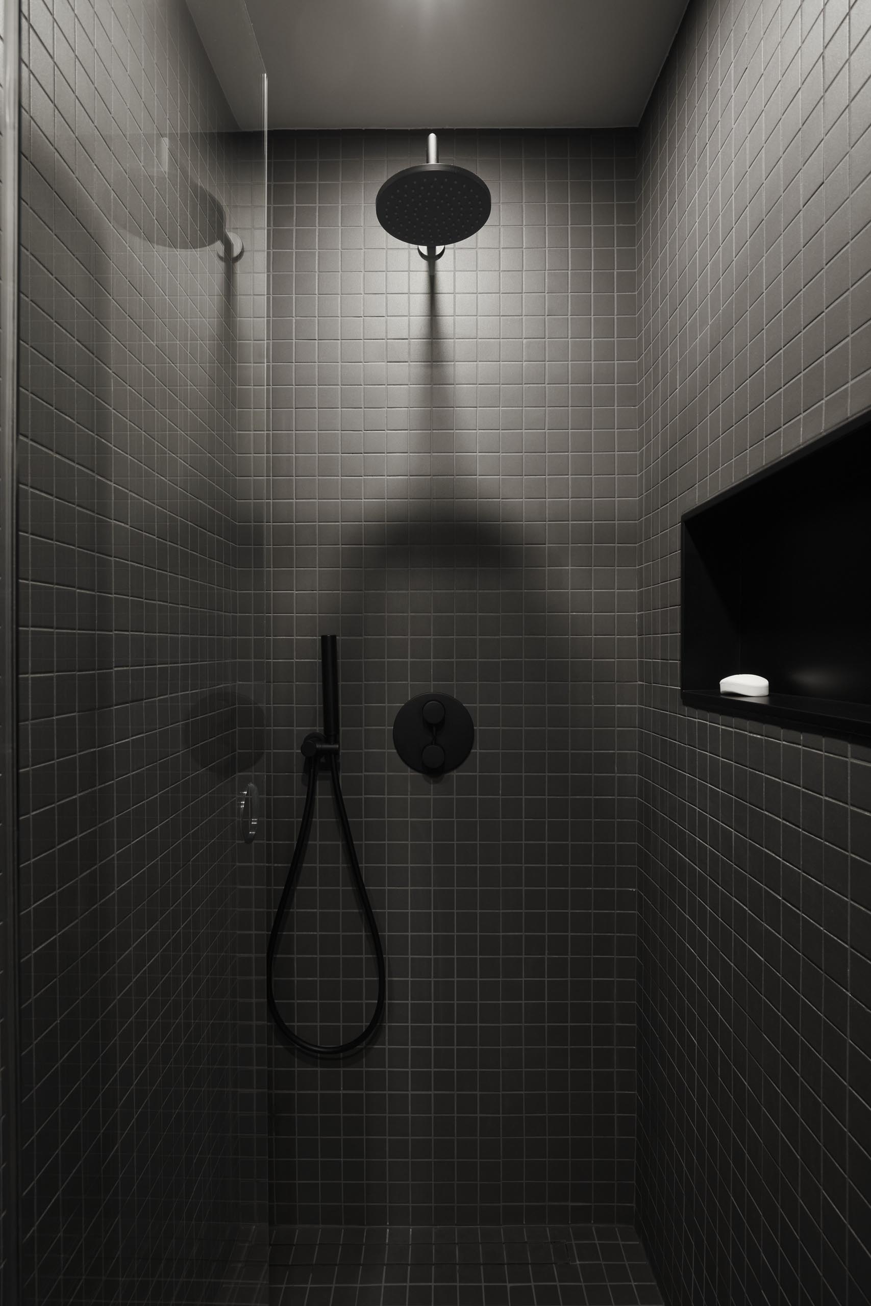 A modern shower with square gray tiles, black hardware, and a shelving niche.