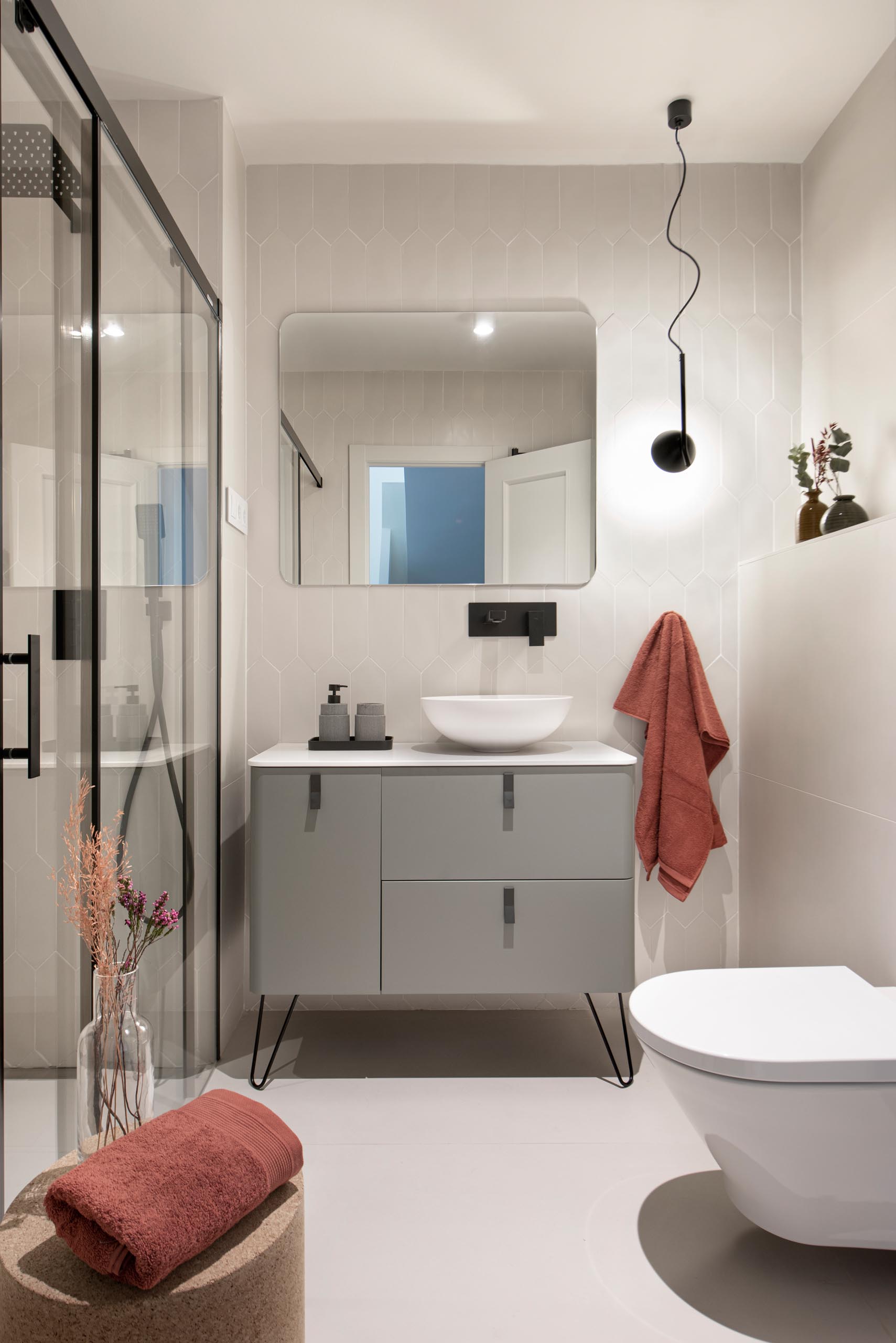 This modern guest bathroom has a simple neutral color palette with a gray vanity, light gray tiles, and black accents.