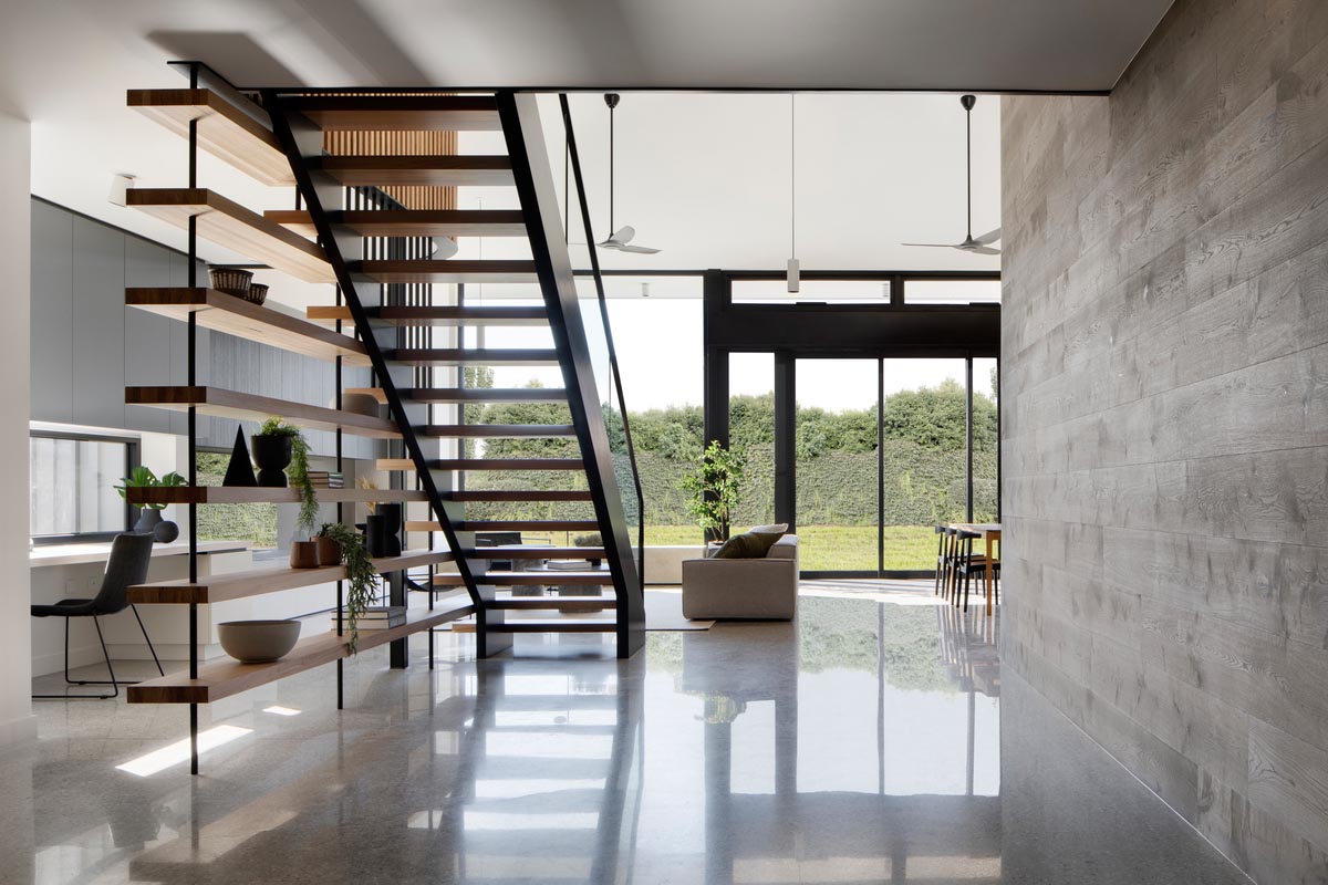 This modern open plan interior includes the living room, home office, dining room, and kitchen, and a polished concrete floor.