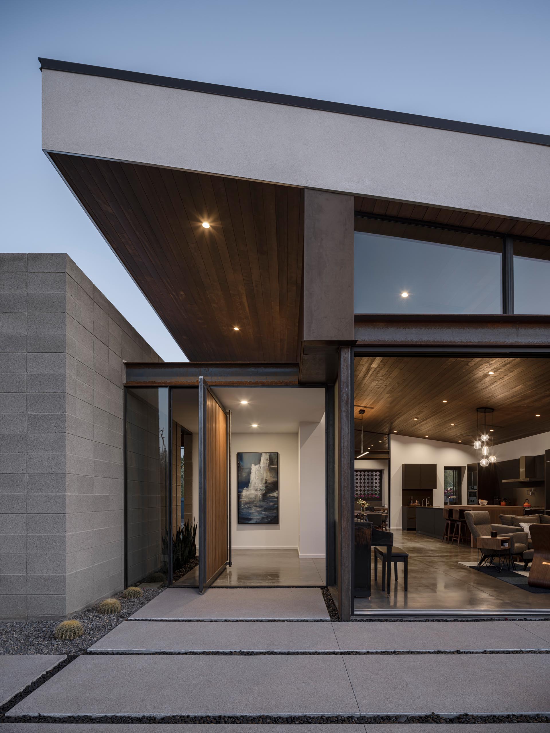 An oversized wood front door with a metal frame pivots to create an eye-catching entryway that opens to a foyer. A small garden is featured on both the exterior and interior of the home.