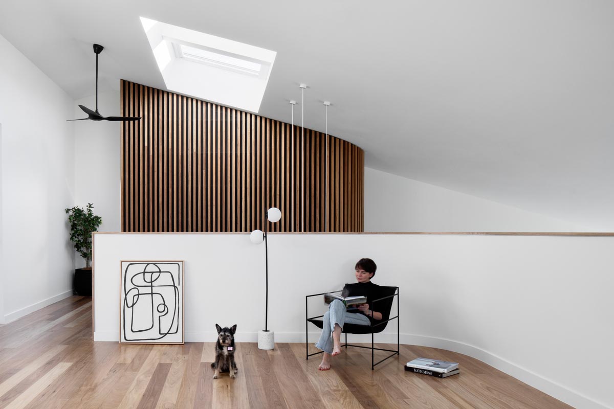 The wood slat wall is visible from an open area with a skylight, and a balcony that overlooks the lower level.