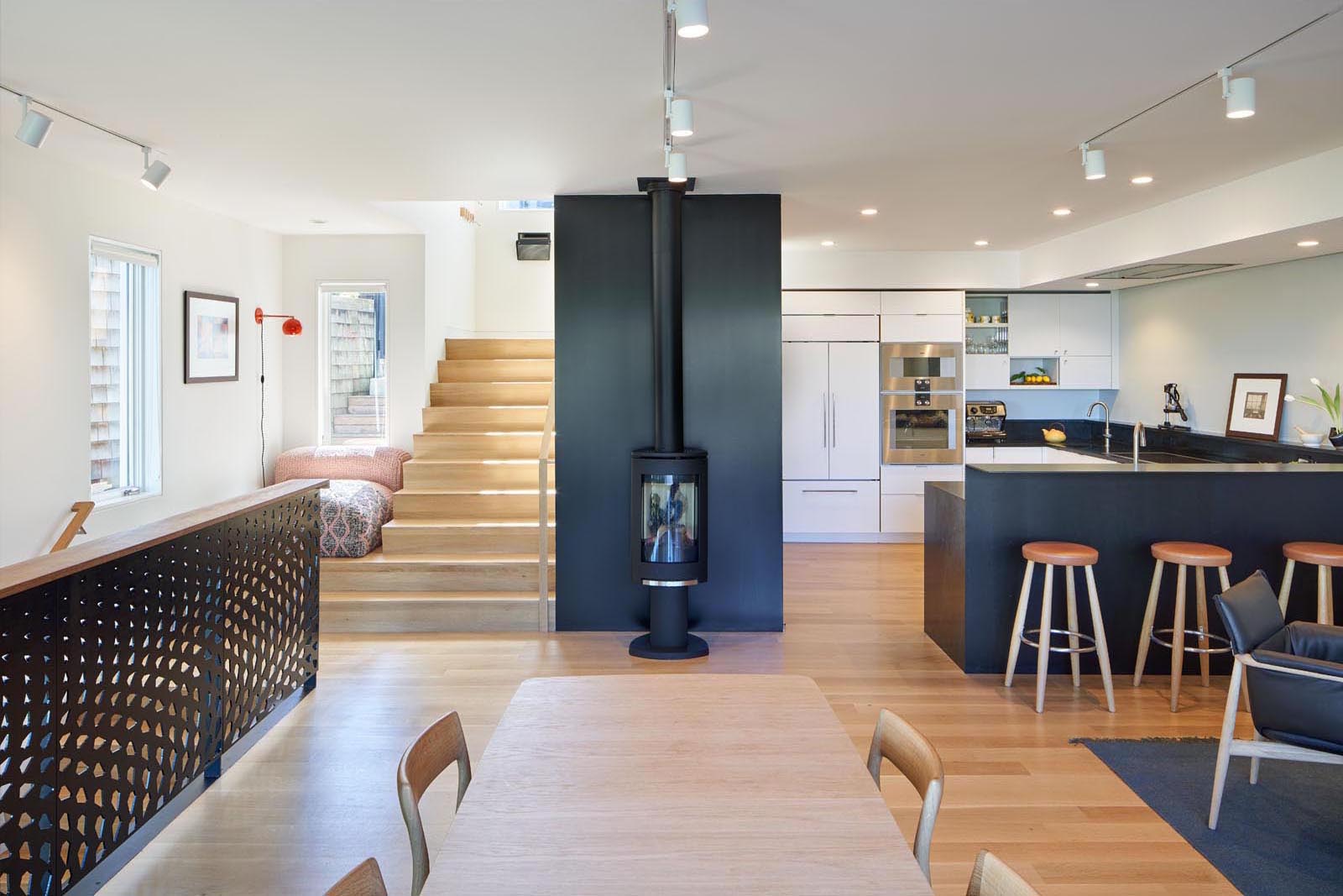 The open plan social areas of this house include the living room, dining room, and kitchen. A black fireplace almost blends in with the black accent wall behind it.