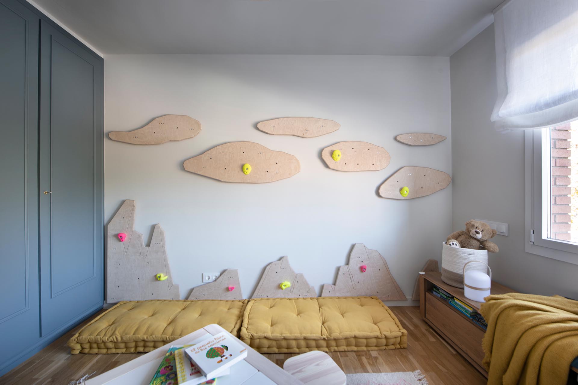 In this modern kid's bedroom, there's uniquely shaped wood cut-outs on the wall that have been designed to attach rock climbing mounts, turning the one empty wall into a climbing wall.