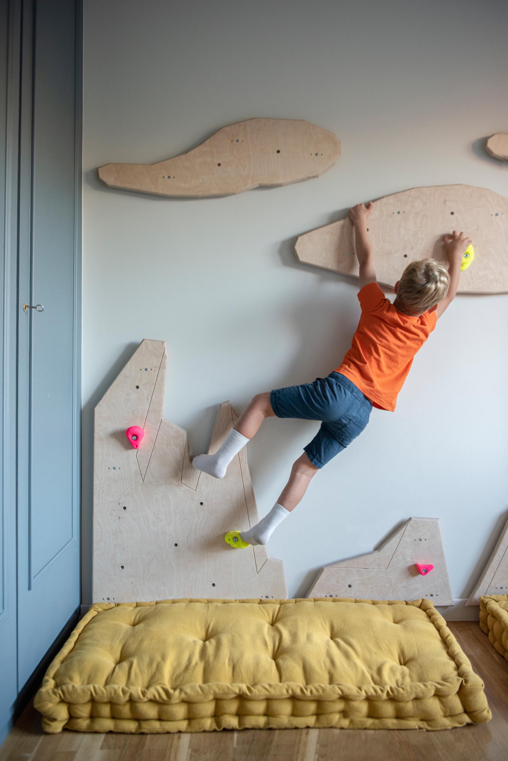In this modern kid's bedroom, there's uniquely shaped wood cut-outs on the wall that have been designed to attach rock climbing mounts, turning the one empty wall into a climbing wall.