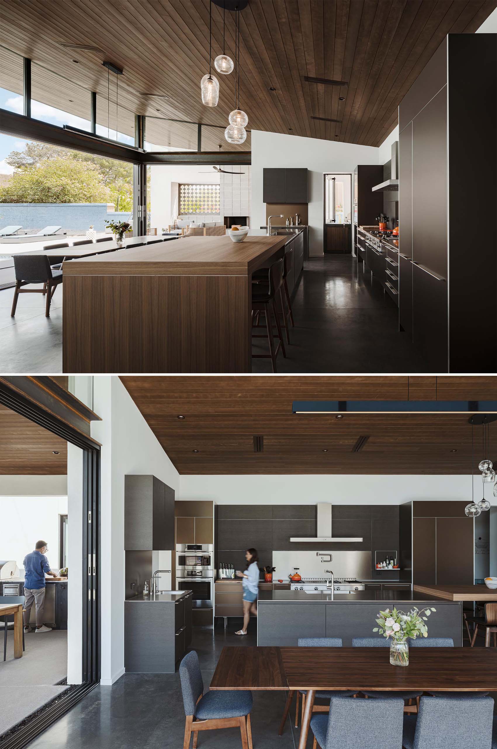 The open plan dining room and kitchen of this modern home includes concrete flooring, a wood dining table, and a large kitchen with an expansive island with a raised section that acts as a bar.