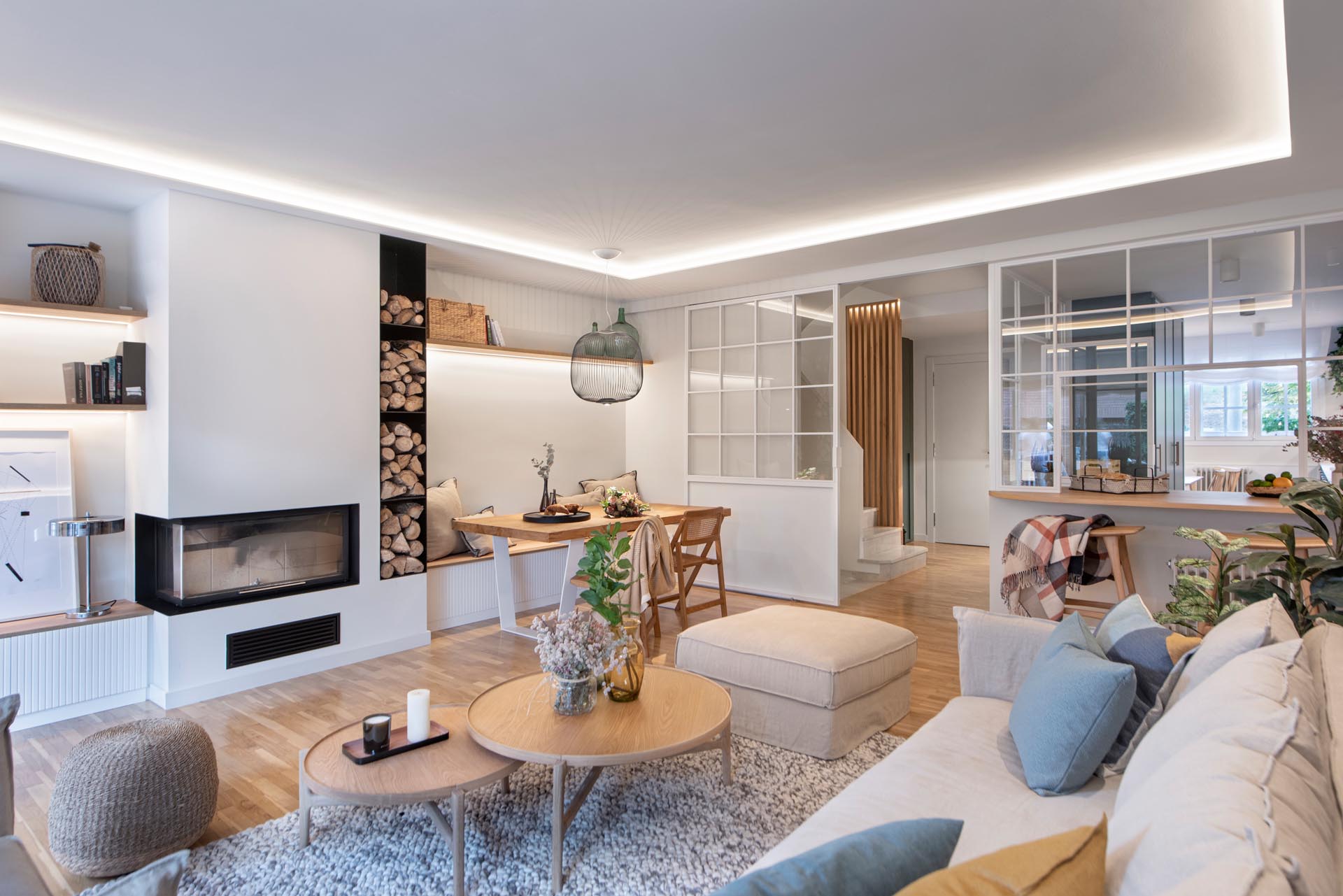 This modern open plan living room has shelving that lines the wall, while the couch and armchair are focused on the fireplace and built-in firewood storage.