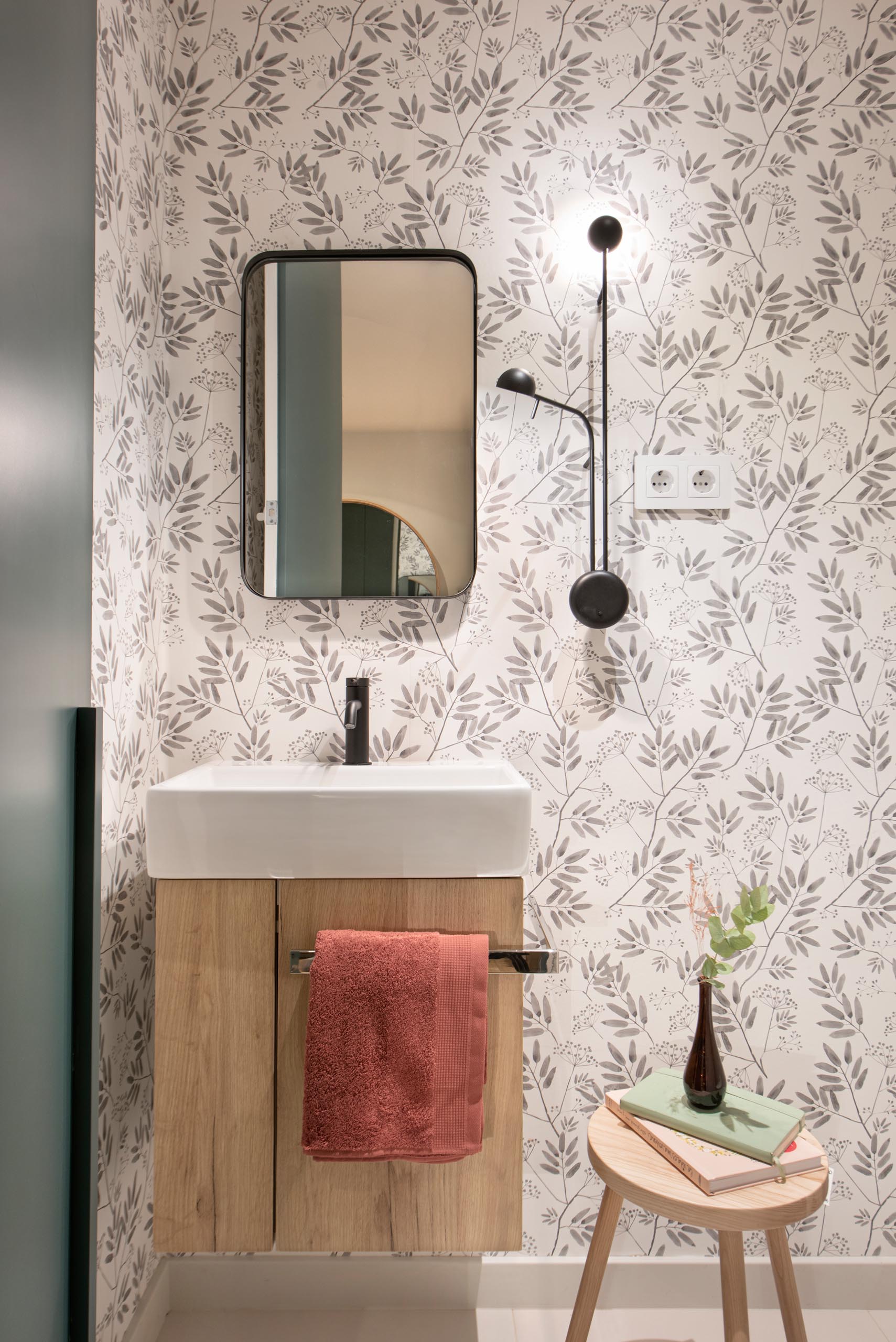 Floral pattern wallpaper, high contrast accessories and taps, and a wall lamp by Ichiro Iwasaki for Vibia, gives this powder room a unique appearance.