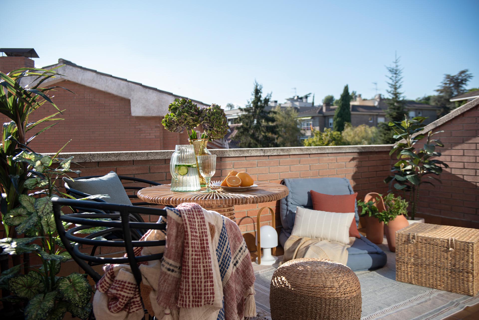 A sliding door opens to a balcony with views of the neighborhood. A small table with chairs, as well as an outdoor rug and low cushion furniture gives the space multiple uses.