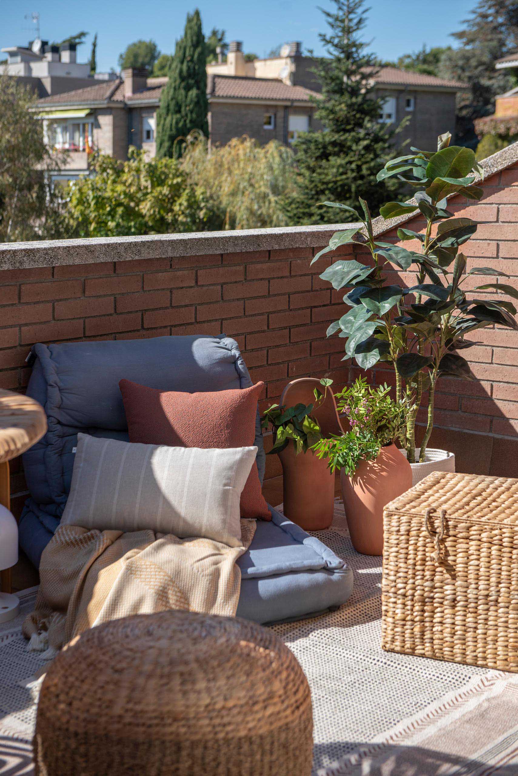 A sliding door opens to a balcony with views of the neighborhood. A small table with chairs, as well as an outdoor rug and low cushion furniture gives the space multiple uses.