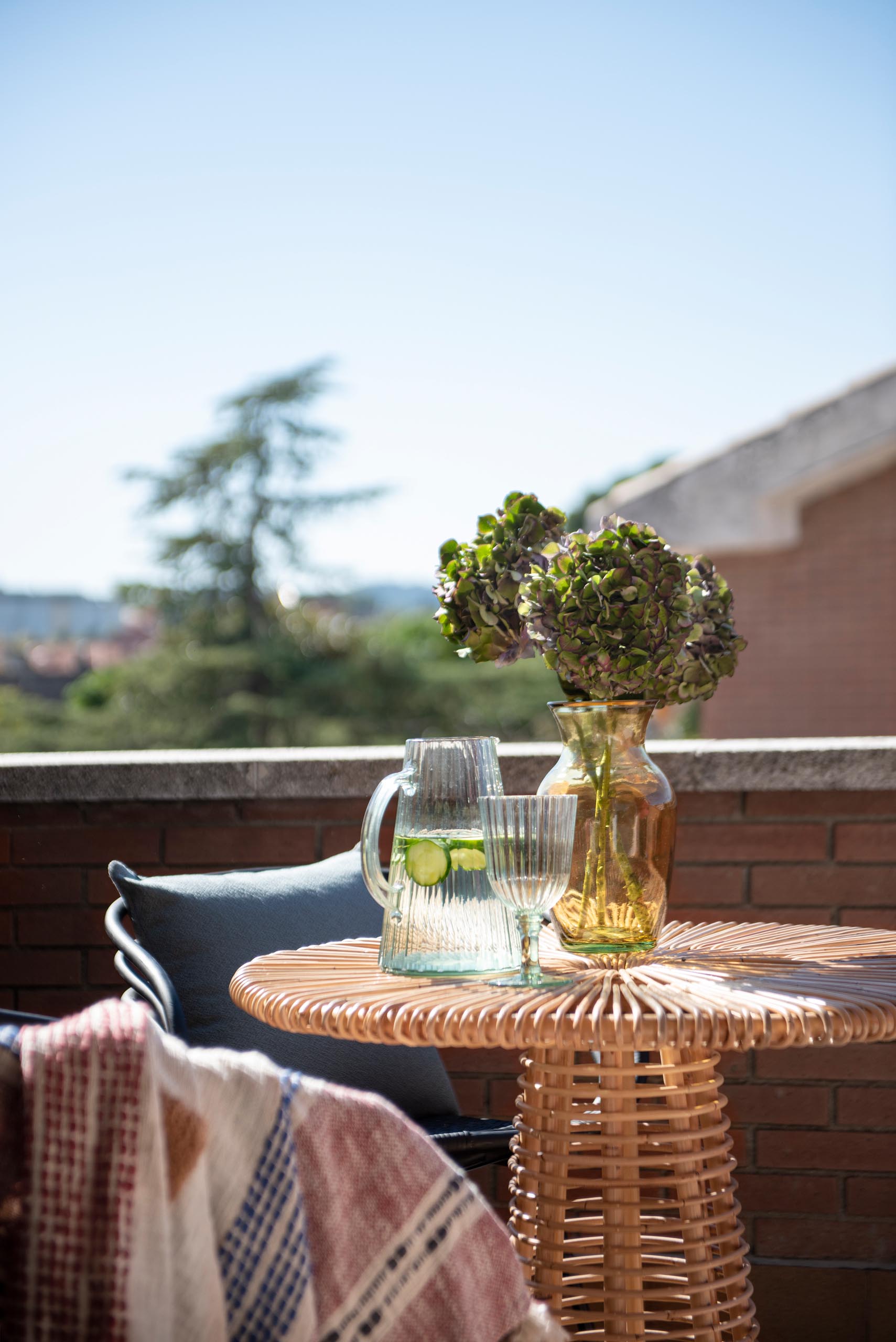 A sliding door opens to a balcony with views of the neighborhood. A small table with chairs, as well as an outdoor rug and low cushion furniture gives the space multiple uses.