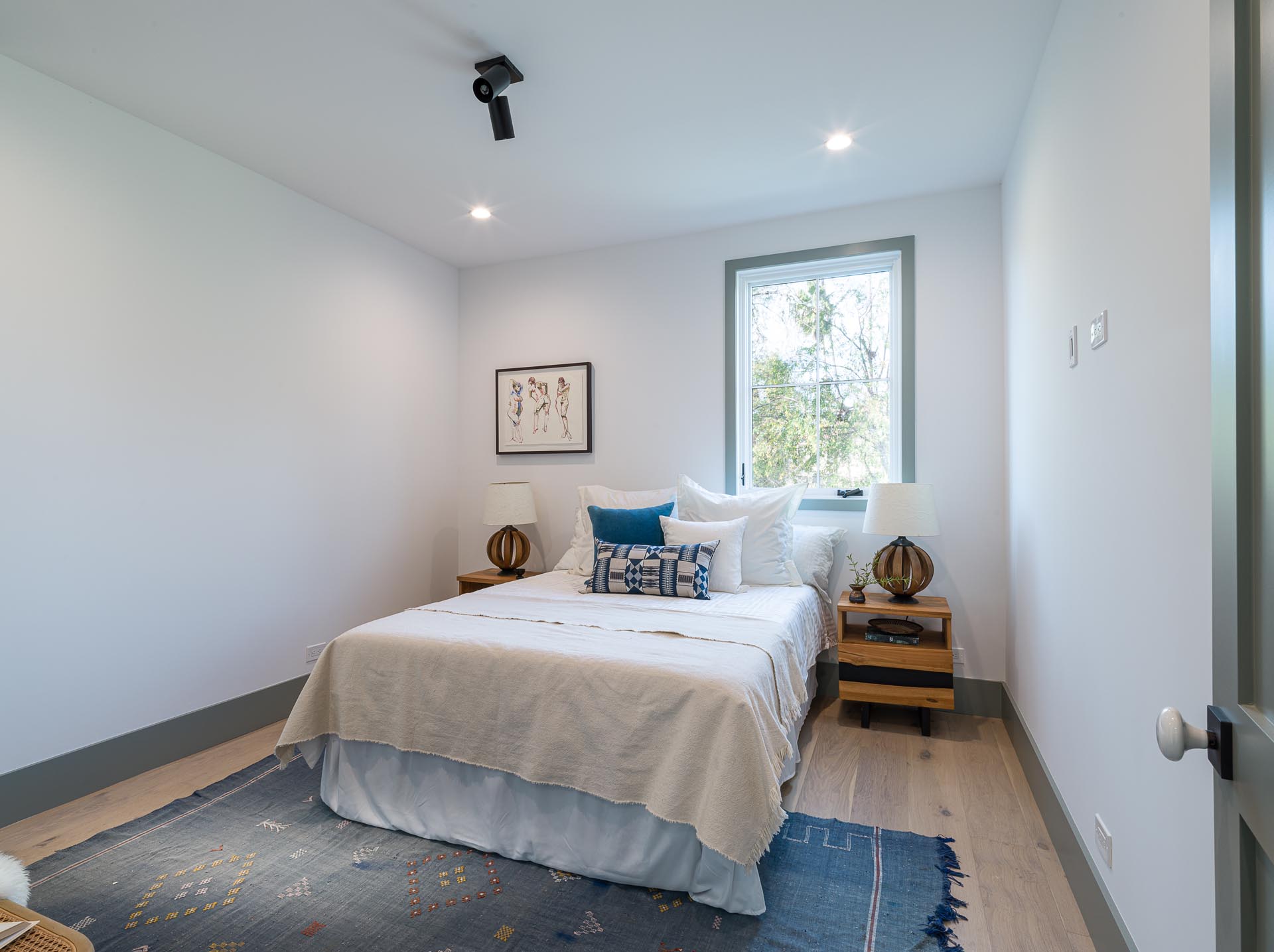 A contemporary bedroom with white walls, wood floors, and gray trim.