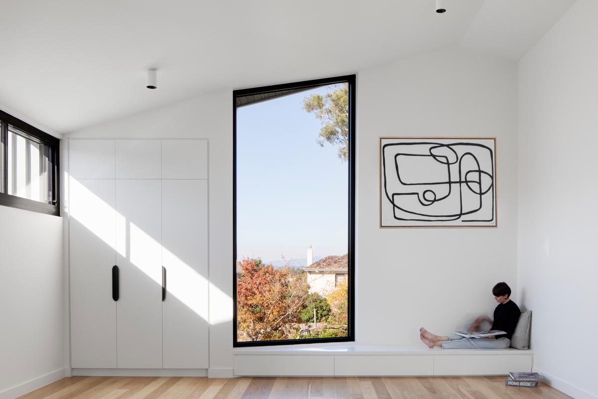 This modern white room has a tall window that's angled, a built-in bench, and built-in closet.