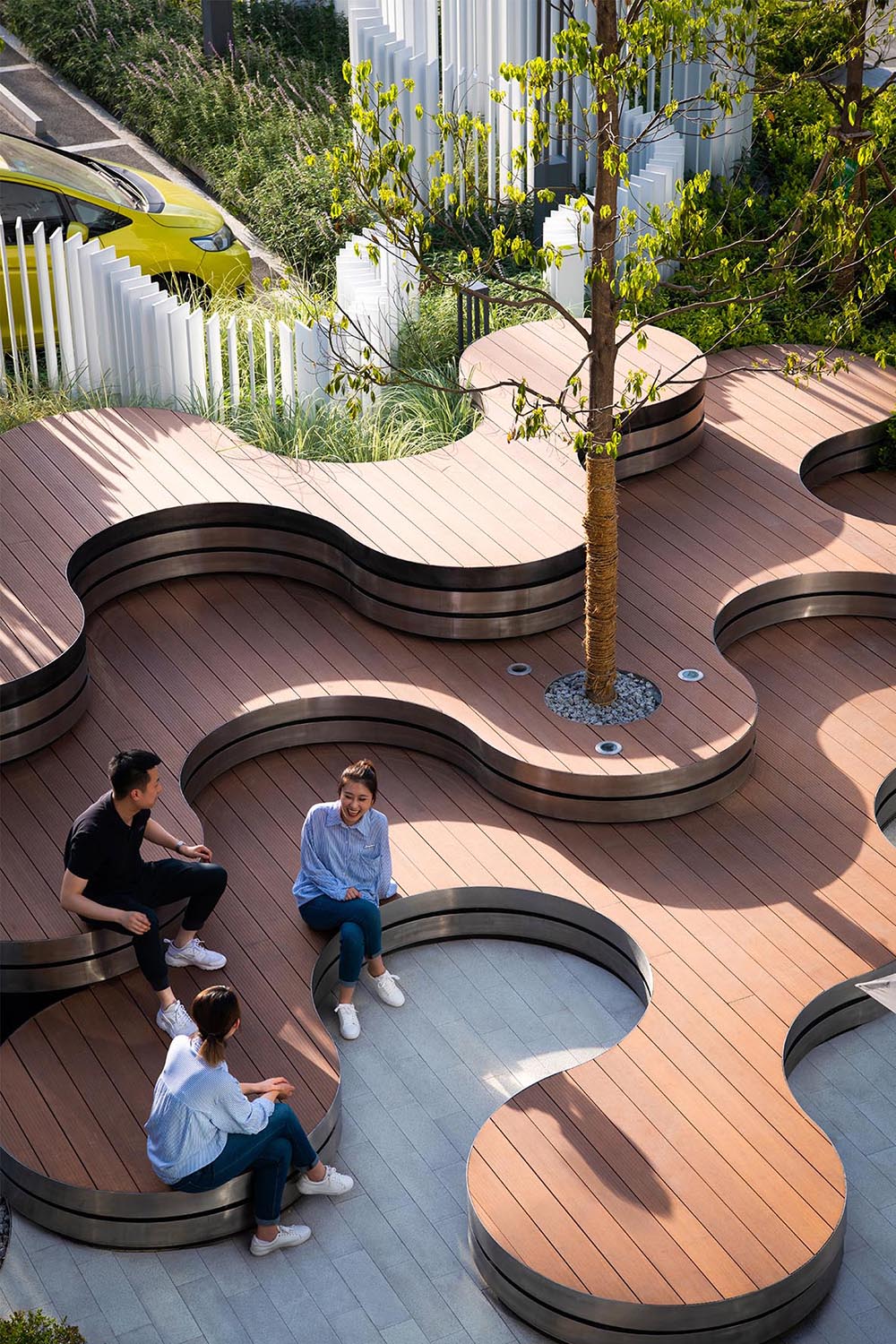 A landscaped park that includes curved tiered seating, a vertical white strip fence, and outdoor lighting.