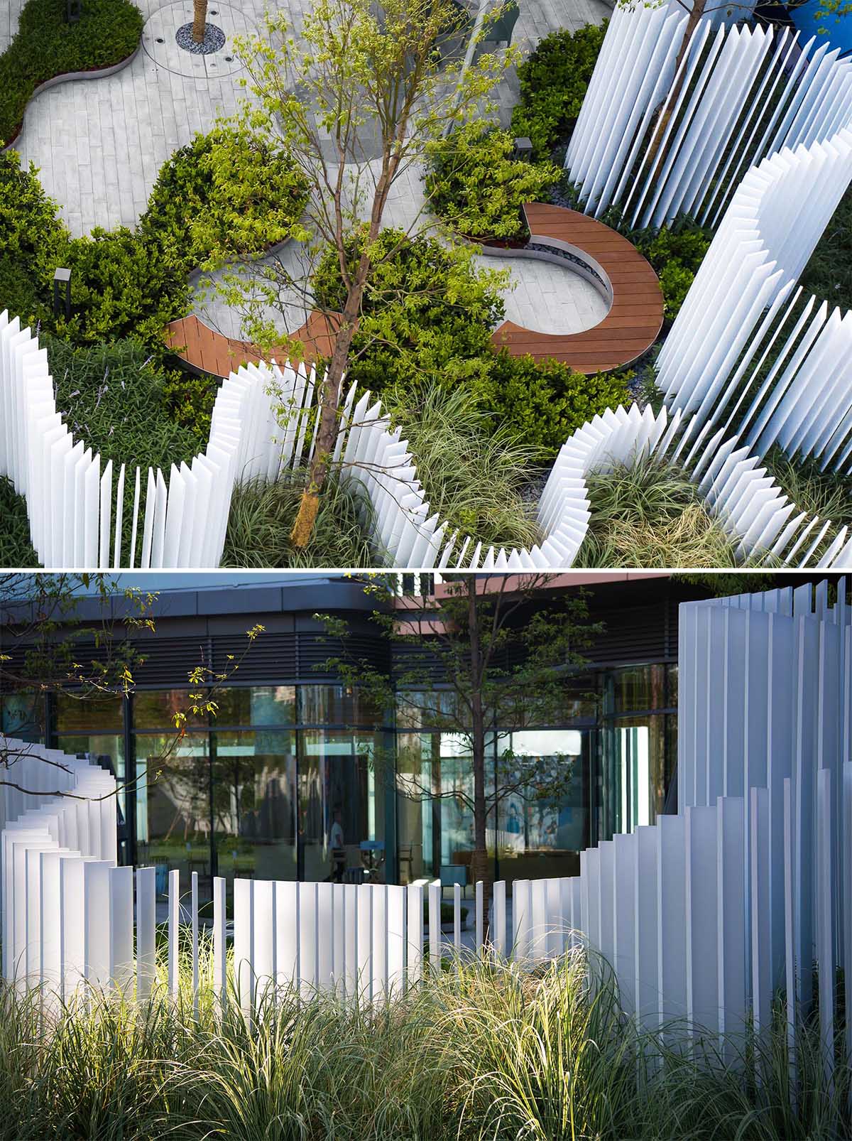 A landscaped park that includes curved seating, and a vertical white strip fence.