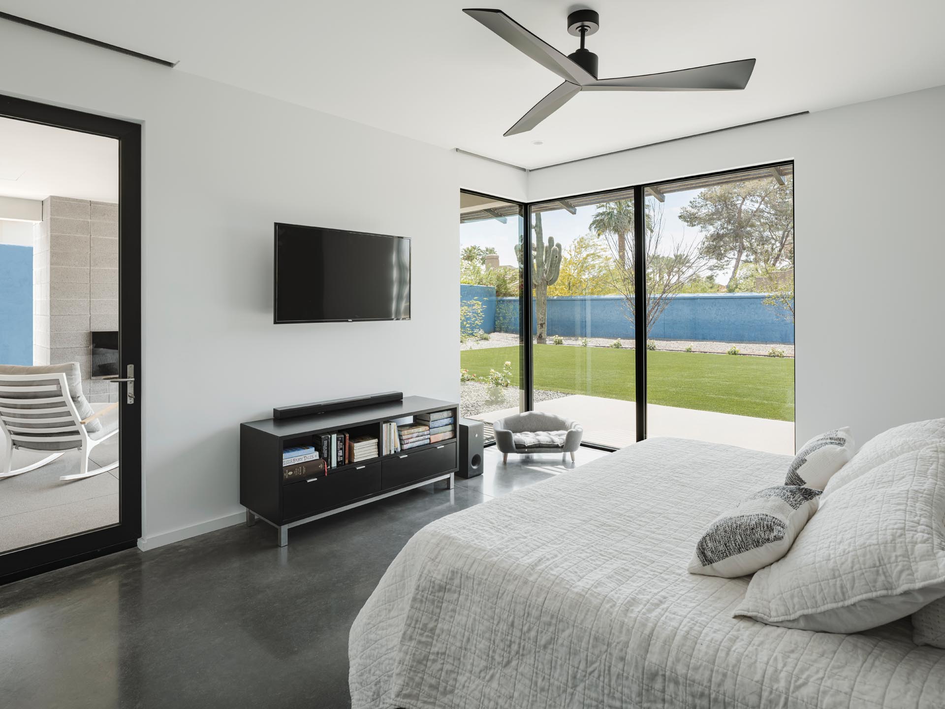 This modern bathroom has concrete floors, white walls, and a door that opens to a private patio with a fireplace.