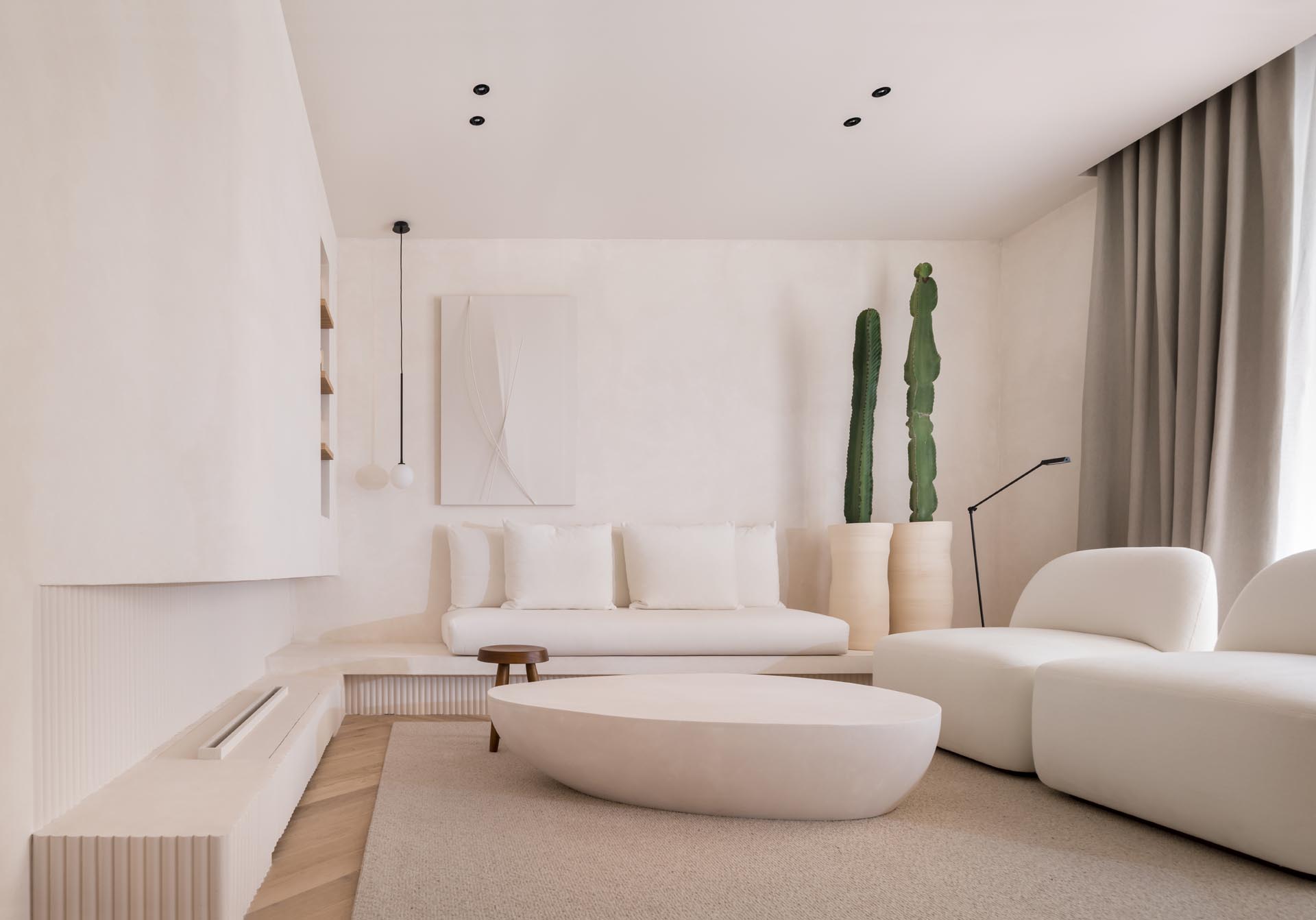 A living room with a simple white color palette, a built-in fireplace, and furniture with curved edges that creates a calm environment with a modern flair.