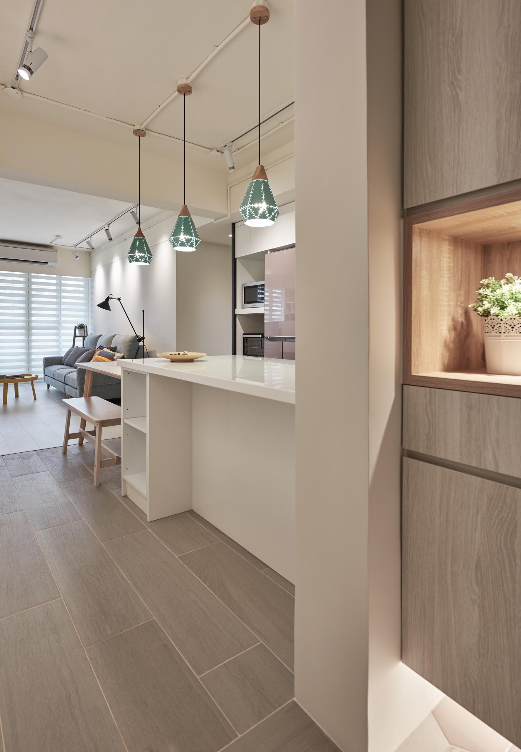 In this apartment kitchen, three pendant lights with a geometric design hang above a peninsula that connects with a dining table, while minimalist hardware-free white kitchen cabinets help to the keep the interior bright.