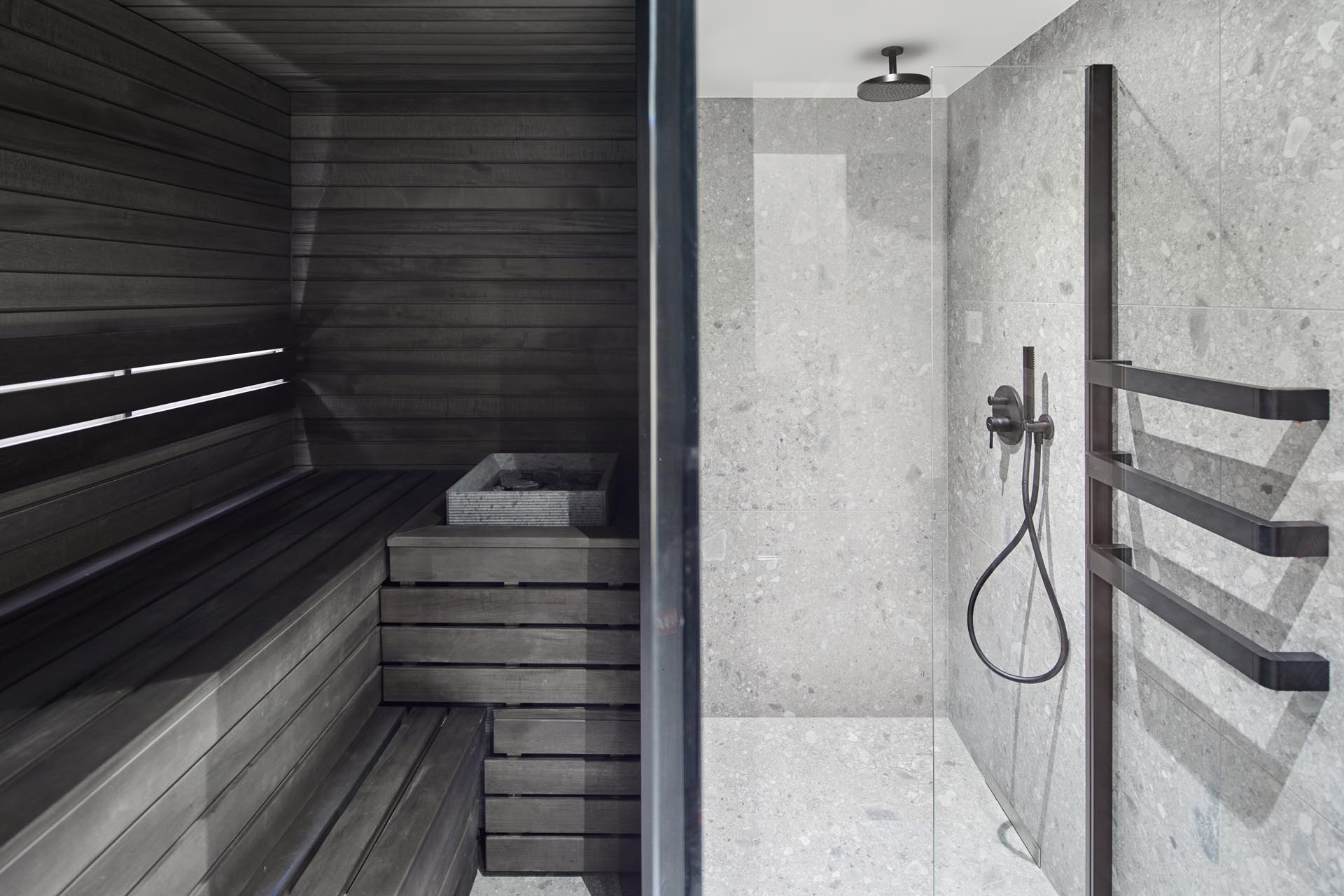 In this modern bathroom, there's blue and dark wood walls, black accents, a walk-in shower, and a sauna.