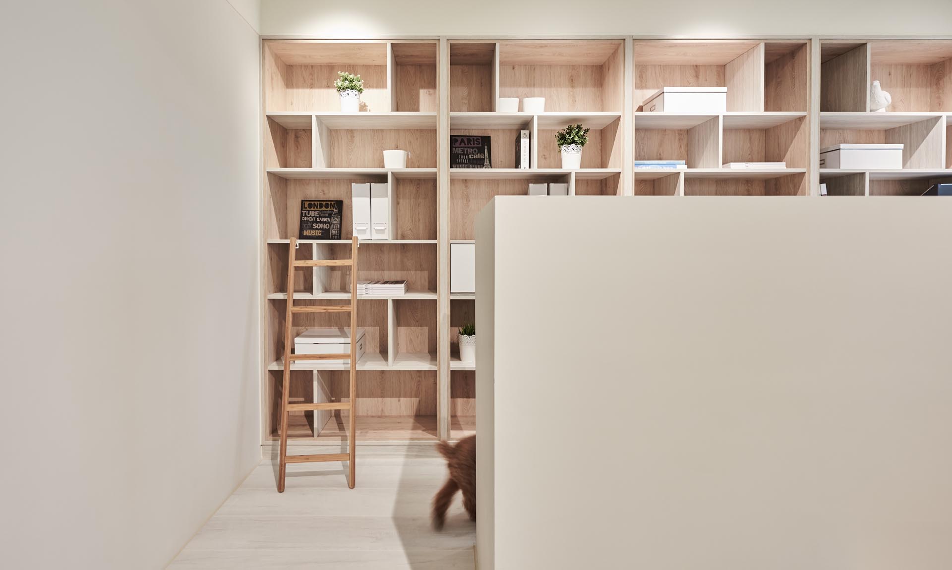 Floor-to-ceiling built-in wood-lined bookshelves provide an abundance of storage for books, folders, plants, and decor items. There's also a small ladder that makes it easy to reach the top shelves.