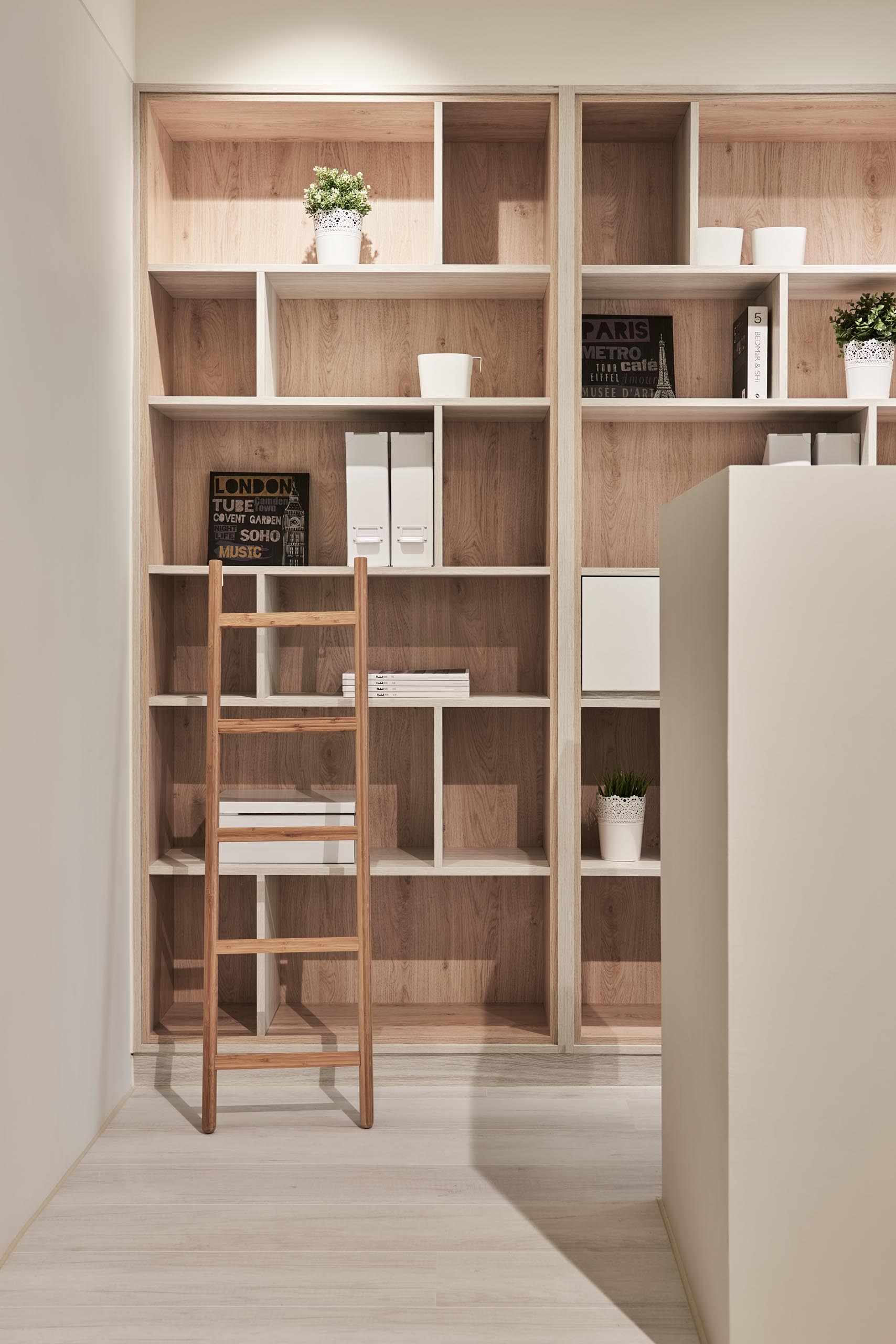 Floor-to-ceiling built-in wood-lined bookshelves provide an abundance of storage for books, folders, plants, and decor items. There's also a small ladder that makes it easy to reach the top shelves.