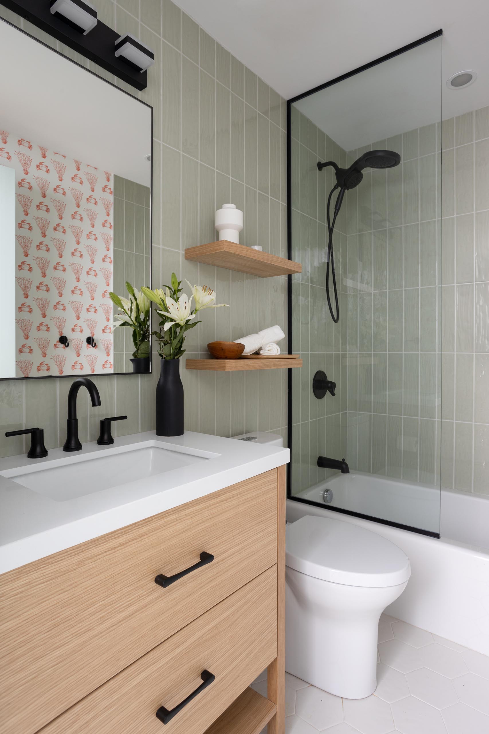 In this bathroom there's black accents and light green tiles that cover the walls, while a wallpaper with a crustacean and coral print adds a quirky colorful touch.