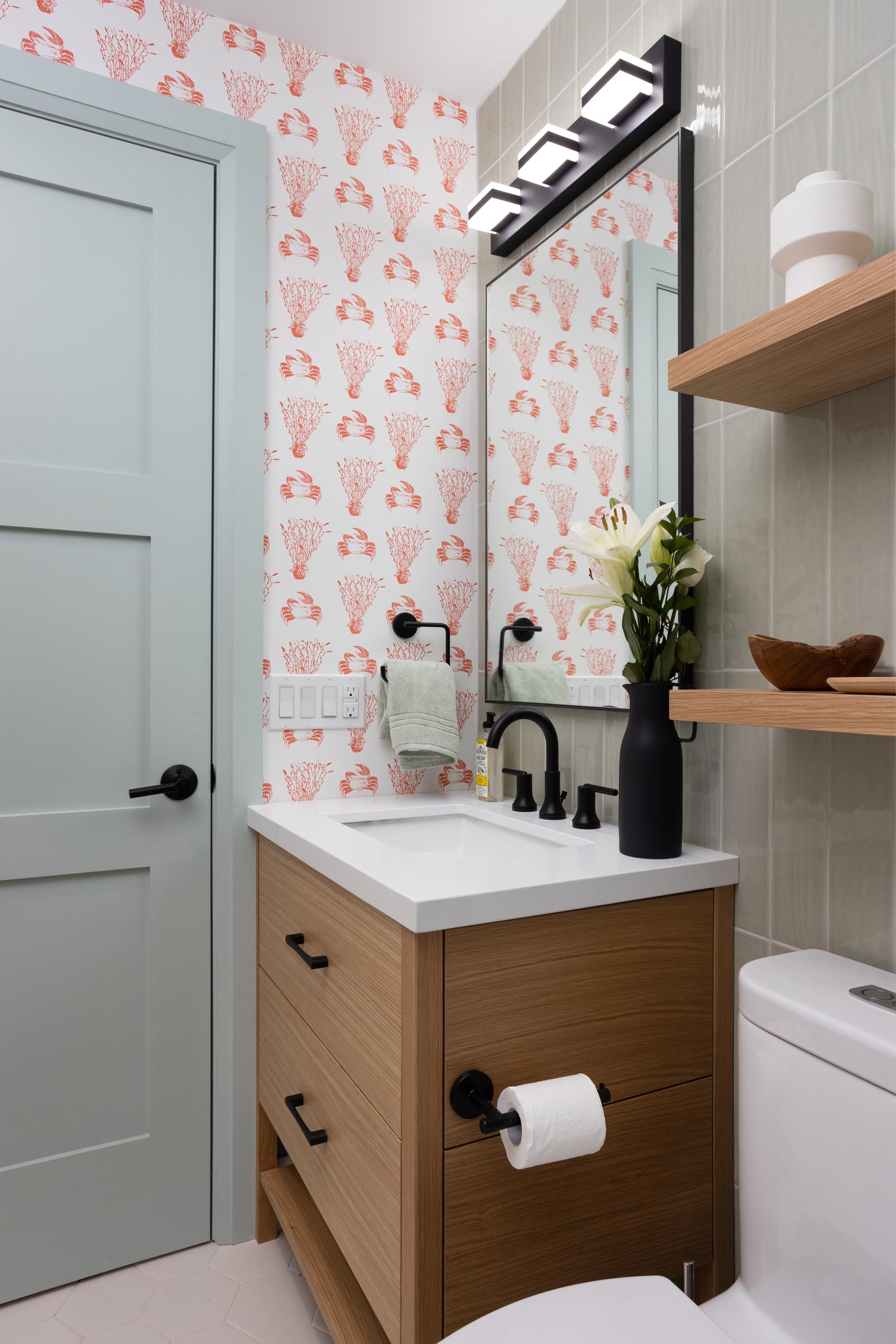 In this bathroom there's black accents and light green tiles that cover the walls, while a wallpaper with a crustacean and coral print adds a quirky colorful touch.