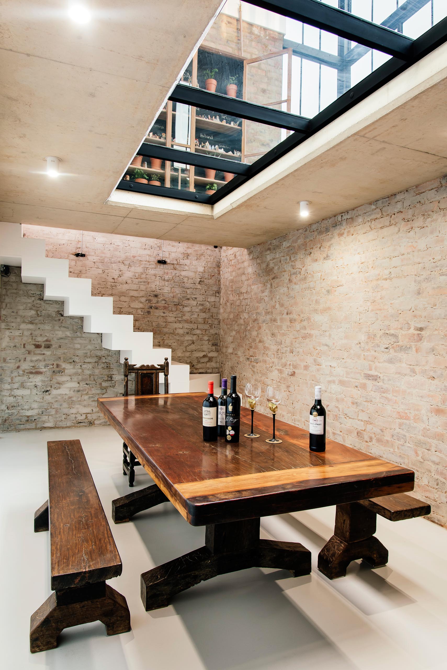 Stairs lead from the conservatory down to the wine cellar via a seamlessly integrated trap door, while a large wood table, which was built by the client, furnishes the room.