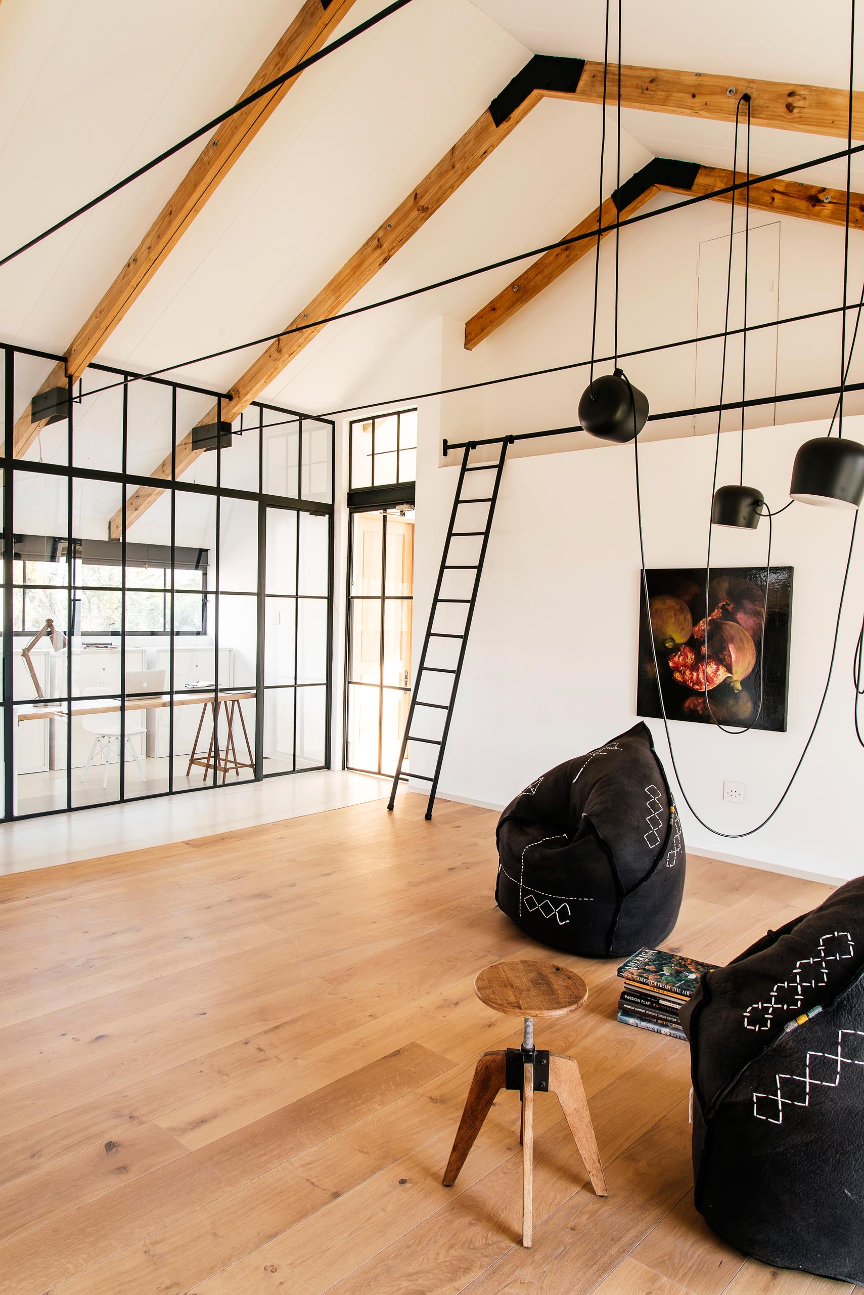 A modern home has a living space with exposed beams, wood flooring, and a pair of black felt chairs.