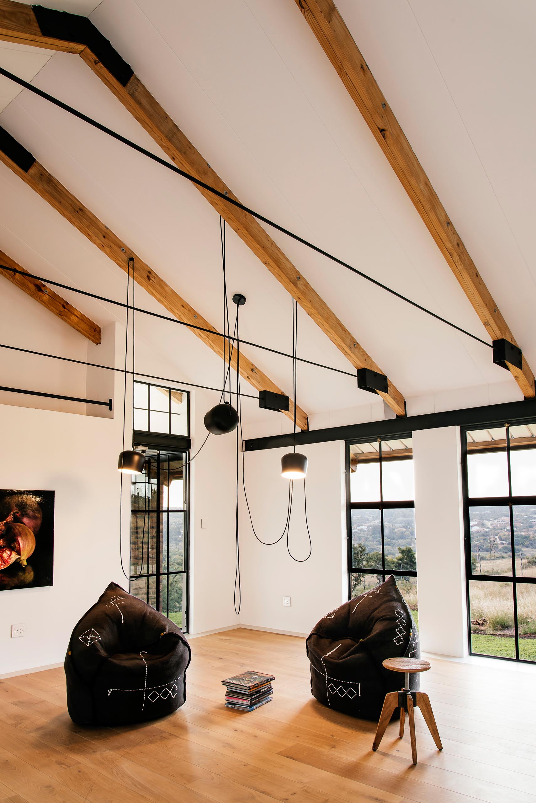 A modern home has a living space with exposed beams, wood flooring, and a pair of black felt chairs.
