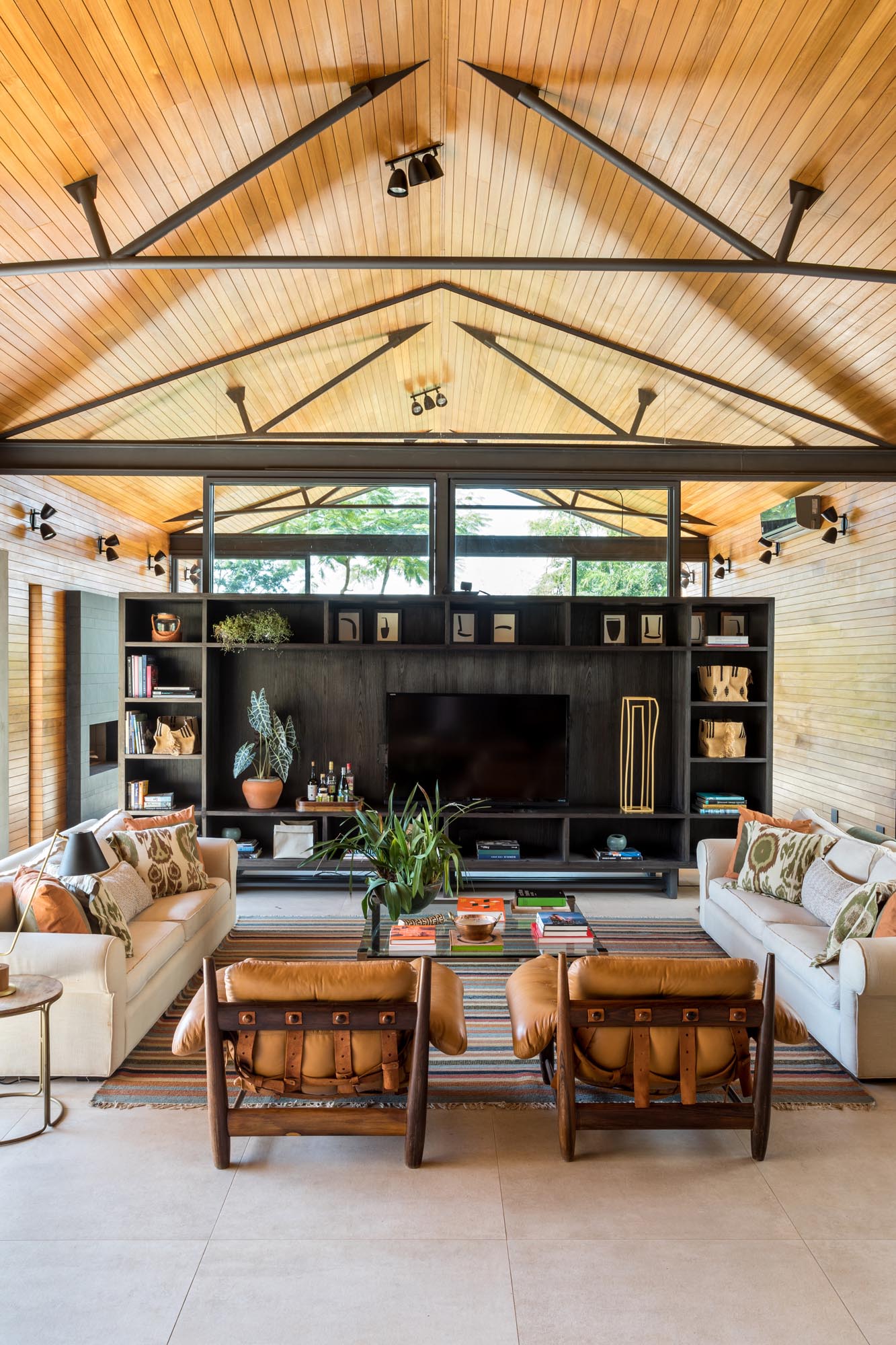 The room divider in this modern home living room, which is made from wood with steel supports, has a wall of shelving with an open area for displaying a television. 