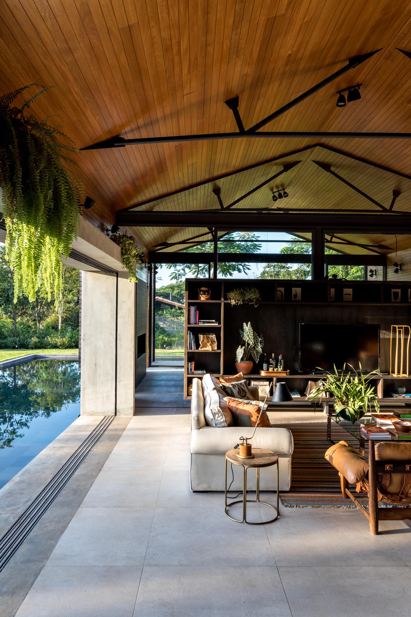 The room divider in this modern home living room, which is made from wood with steel supports, has a wall of shelving with an open area for displaying a television. 