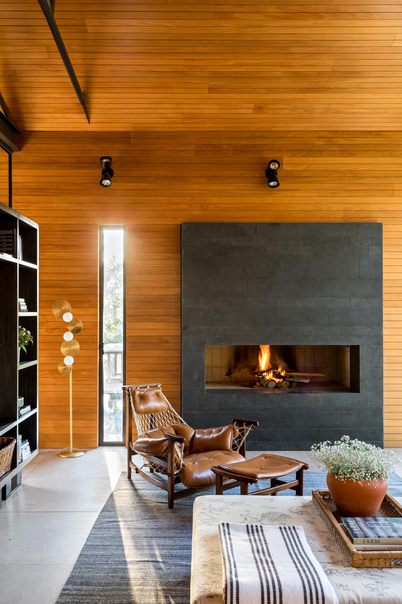 This modern living room is open to the swimming pool, and is furnished with a pair of couches, armchairs, and a fireplace. The room divider is a mirror image of the other side, with shelving and a mounted TV.