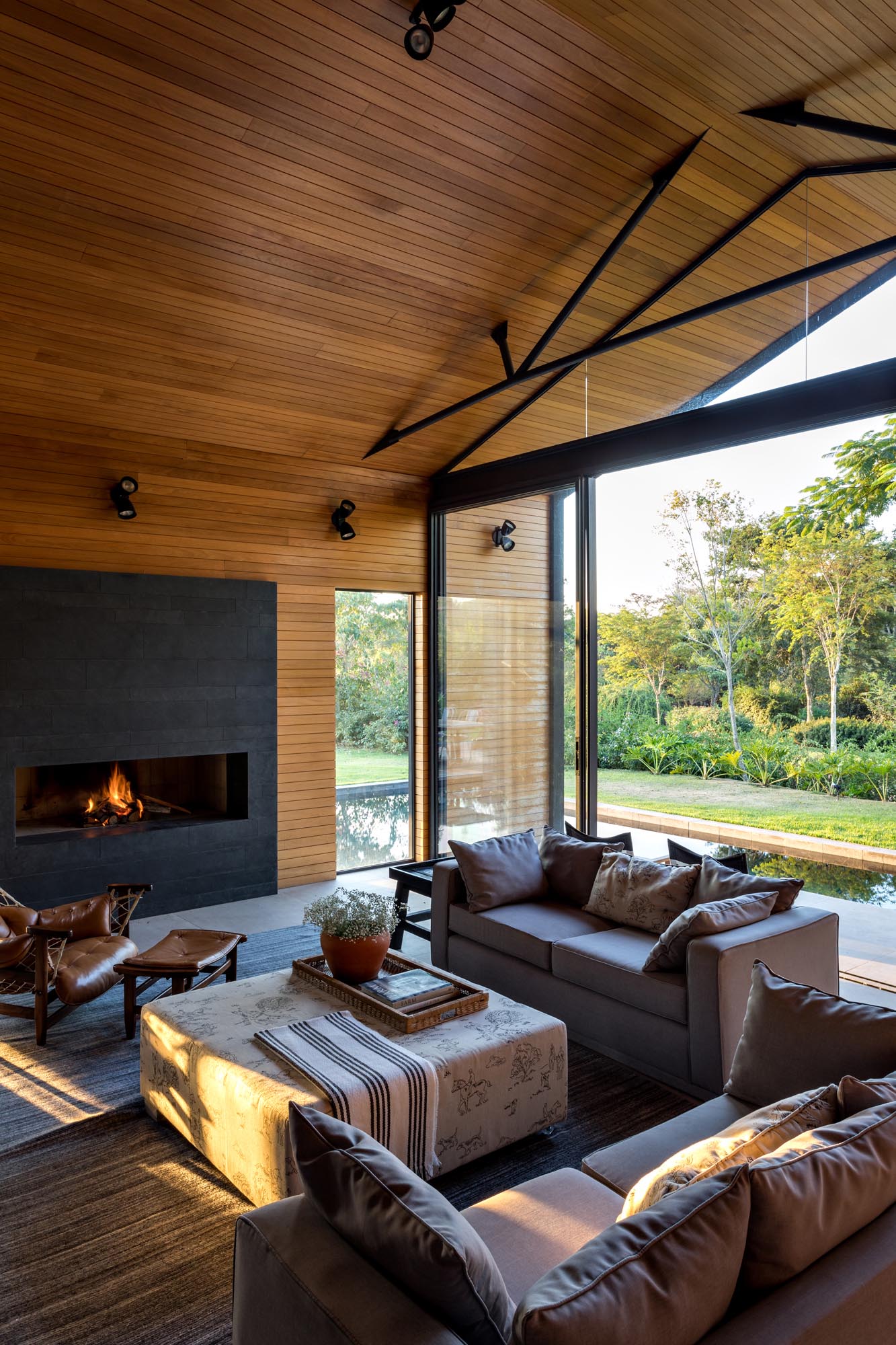 This modern living room is open to the swimming pool, and is furnished with a pair of couches, armchairs, and a fireplace.