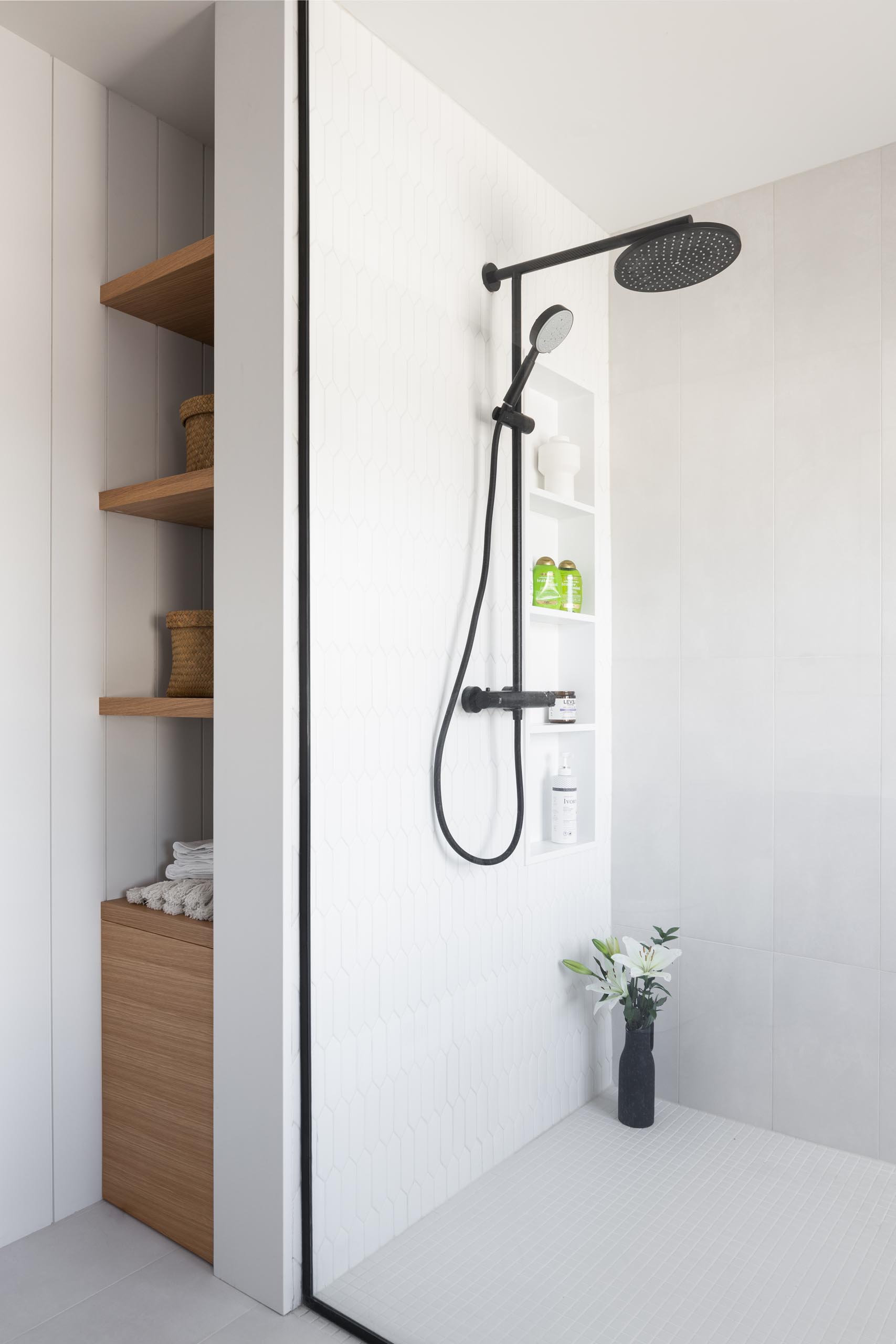 A modern bathroom with white picket-style tiles, a shelving niche, and built-in wood shelves.