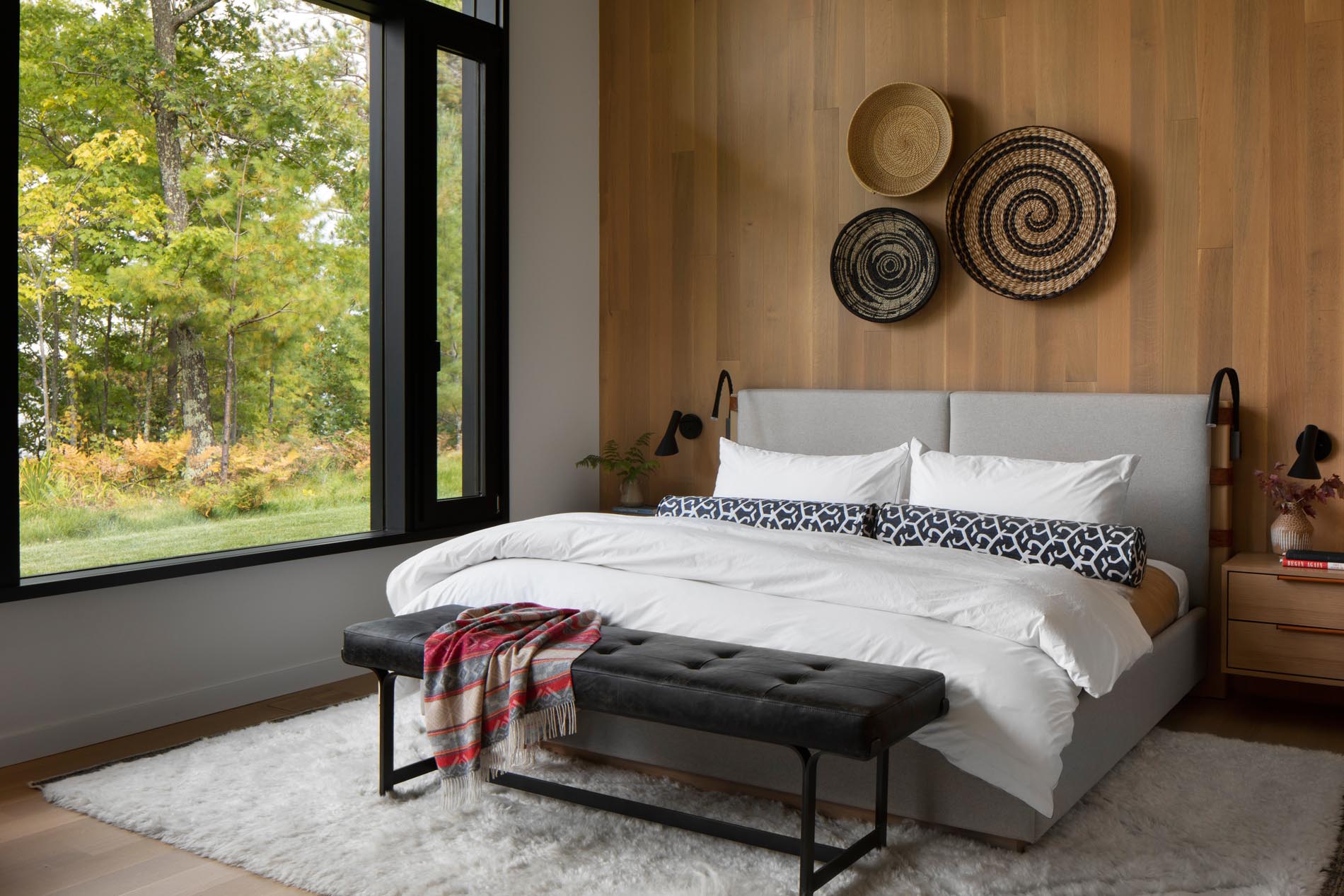 This modern bedroom has a floor-to-ceiling wood accent wall adorned with woven baskets, provides a backdrop for an upholstered gray bed.