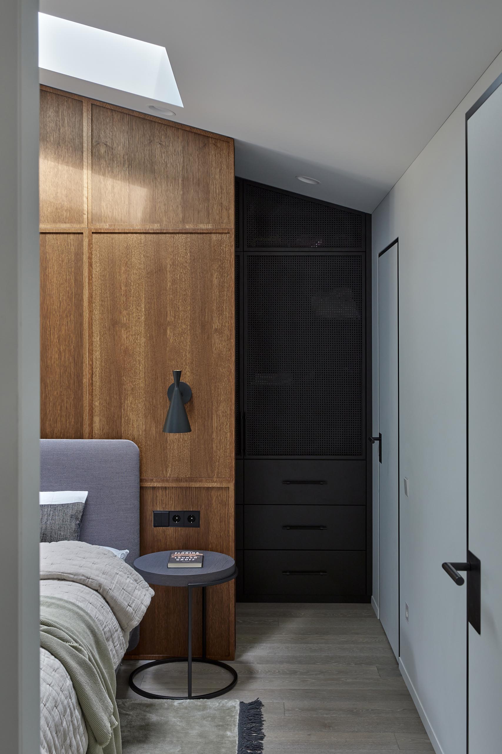 In is modern primary bedroom, there's yet another wood accent wall, this time, providing a backdrop for the gray upholstered bed, while the dark cabinetry of the wardrobe provides a contrasting element in the room.