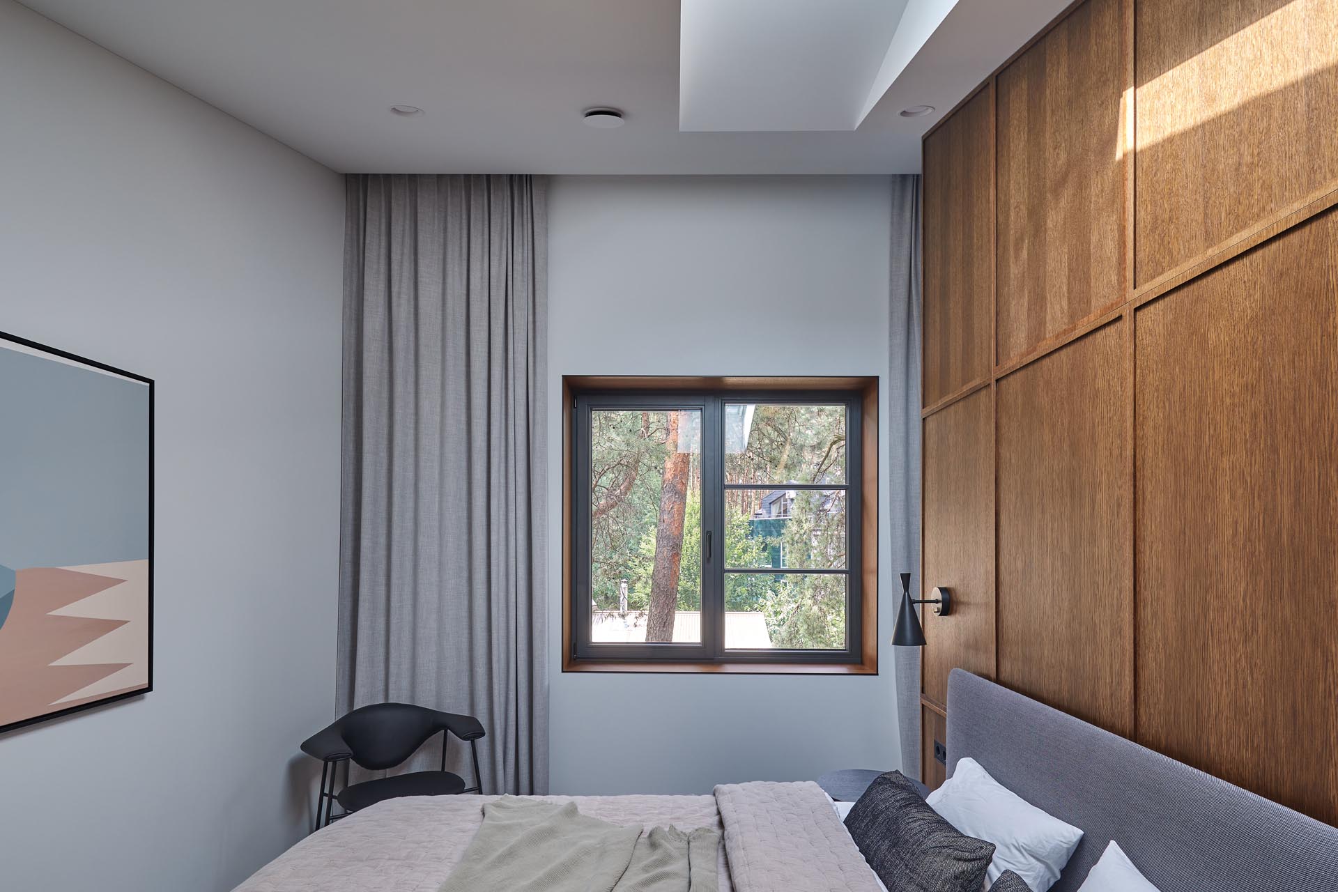 In is modern primary bedroom, there's yet another wood accent wall, this time, providing a backdrop for the gray upholstered bed, while the dark cabinetry of the wardrobe provides a contrasting element in the room.