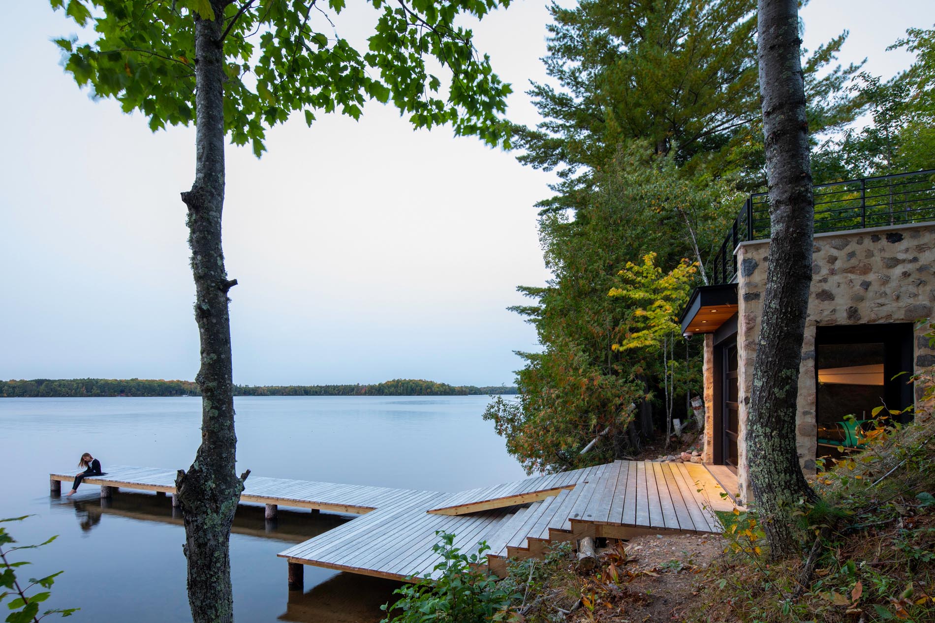 This modern home includes steps that lead down to a boathouse with a rooftop deck, as well as a dock.