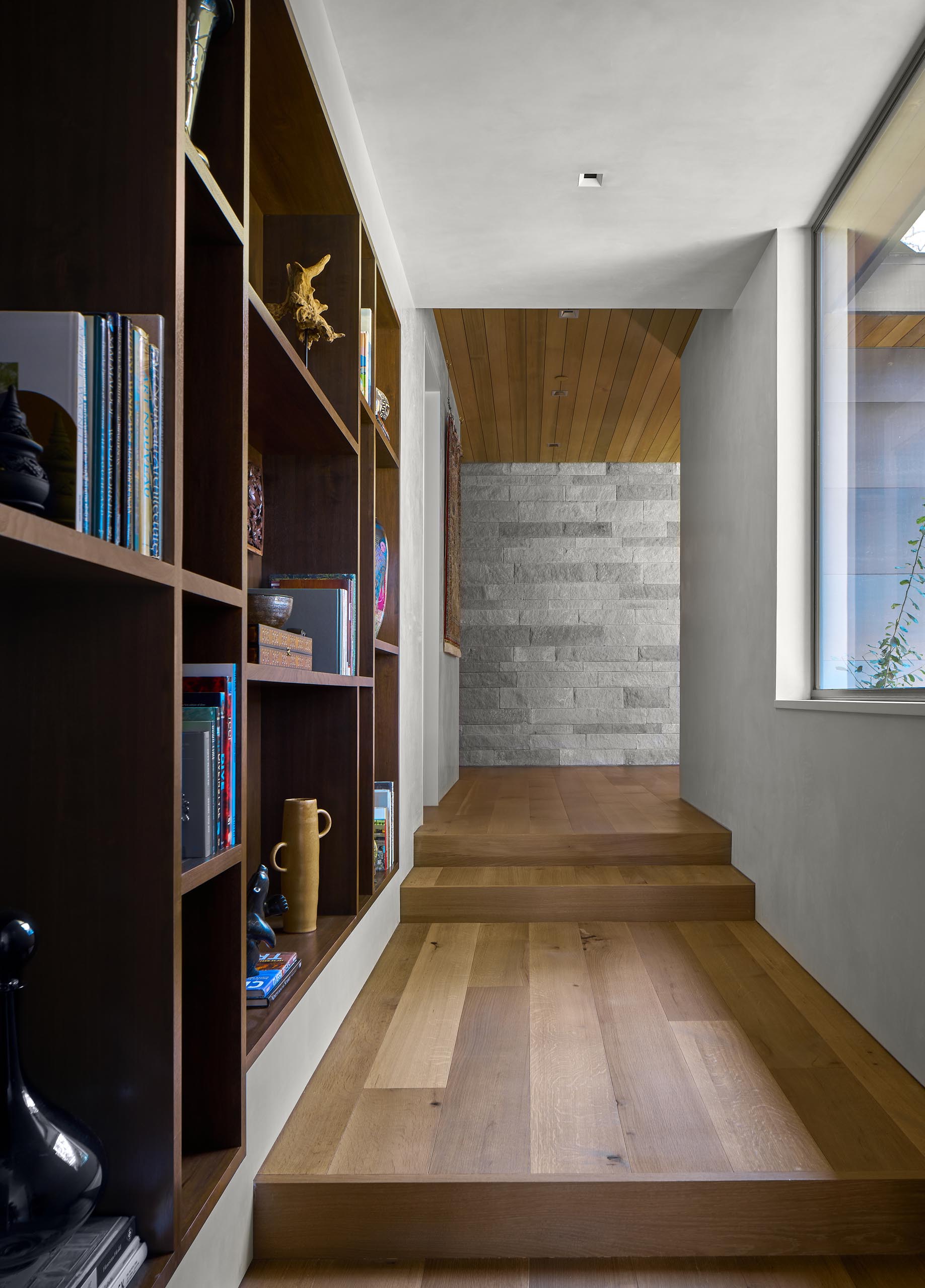 A hallway with wood flooring and built-in shelving connects the various areas of the home.