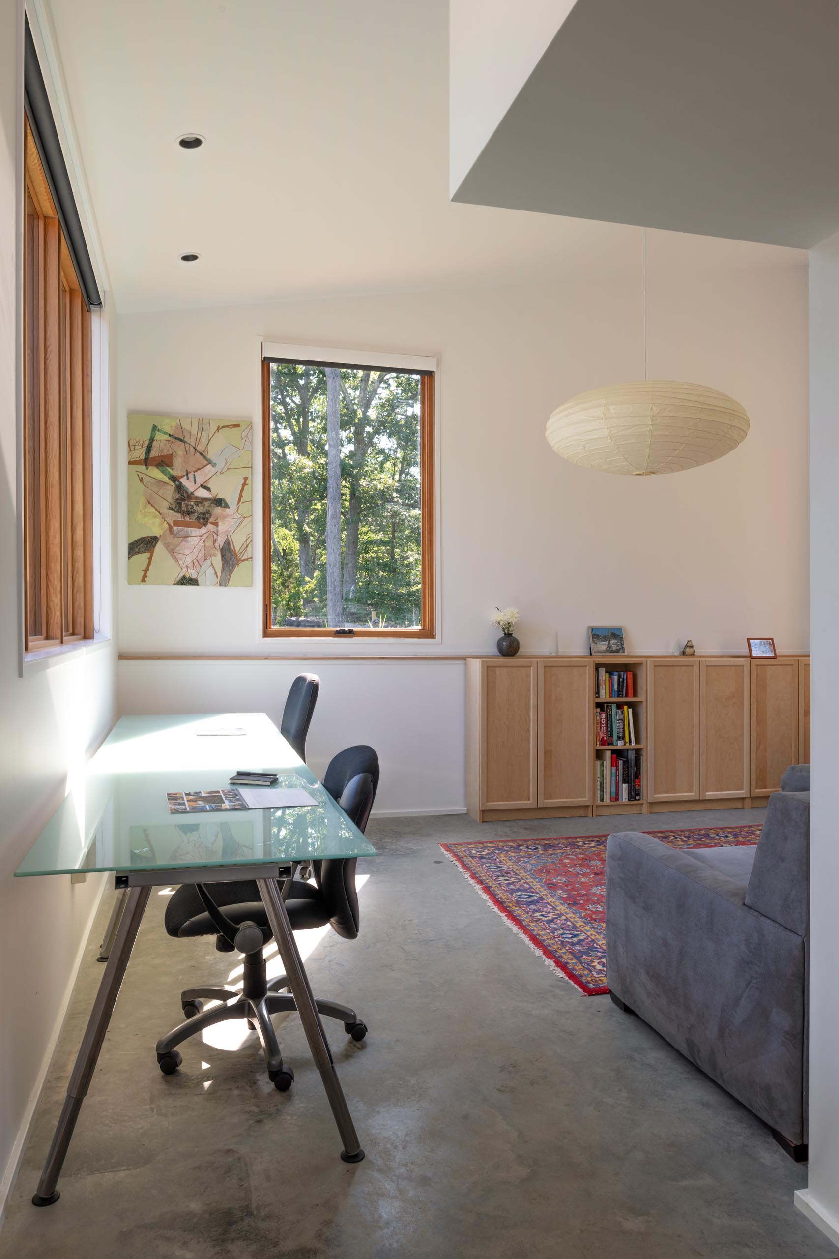 A home office with room for multiple people to work includes a long desk by the window, a couch, and storage cabinets.