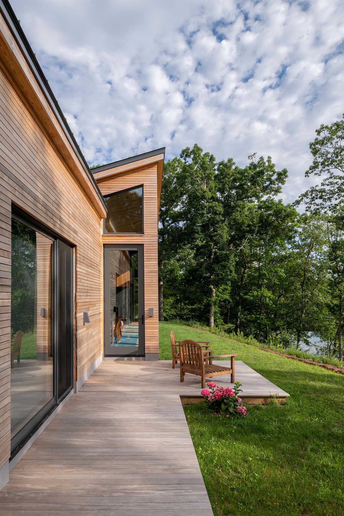 A deck wraps around this modern home, while the charcoal-colored window frames provide a contrast to the wood and complement the metal roof and garage door.