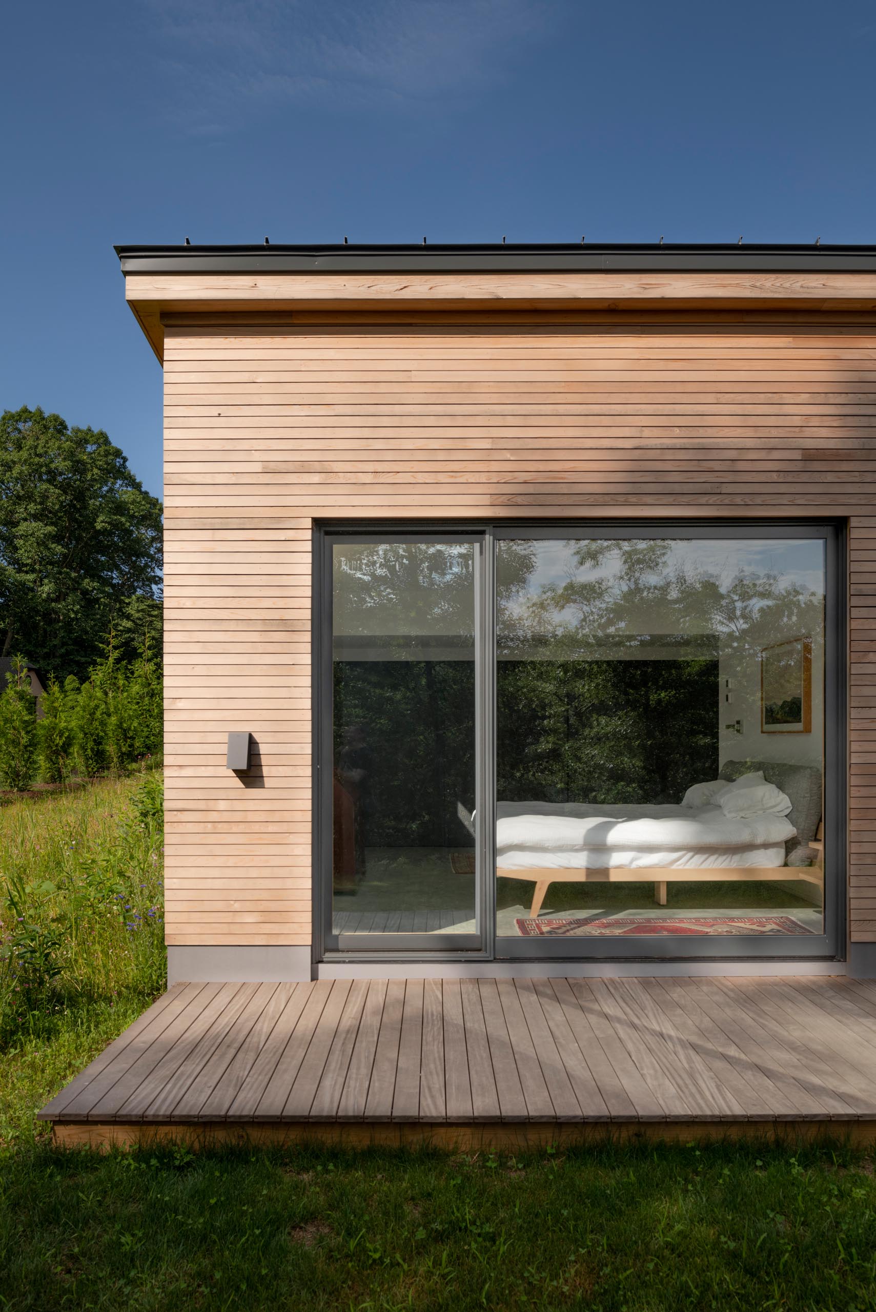 A deck wraps around this modern home, while the charcoal-colored window frames provide a contrast to the wood and complement the metal roof and garage door.