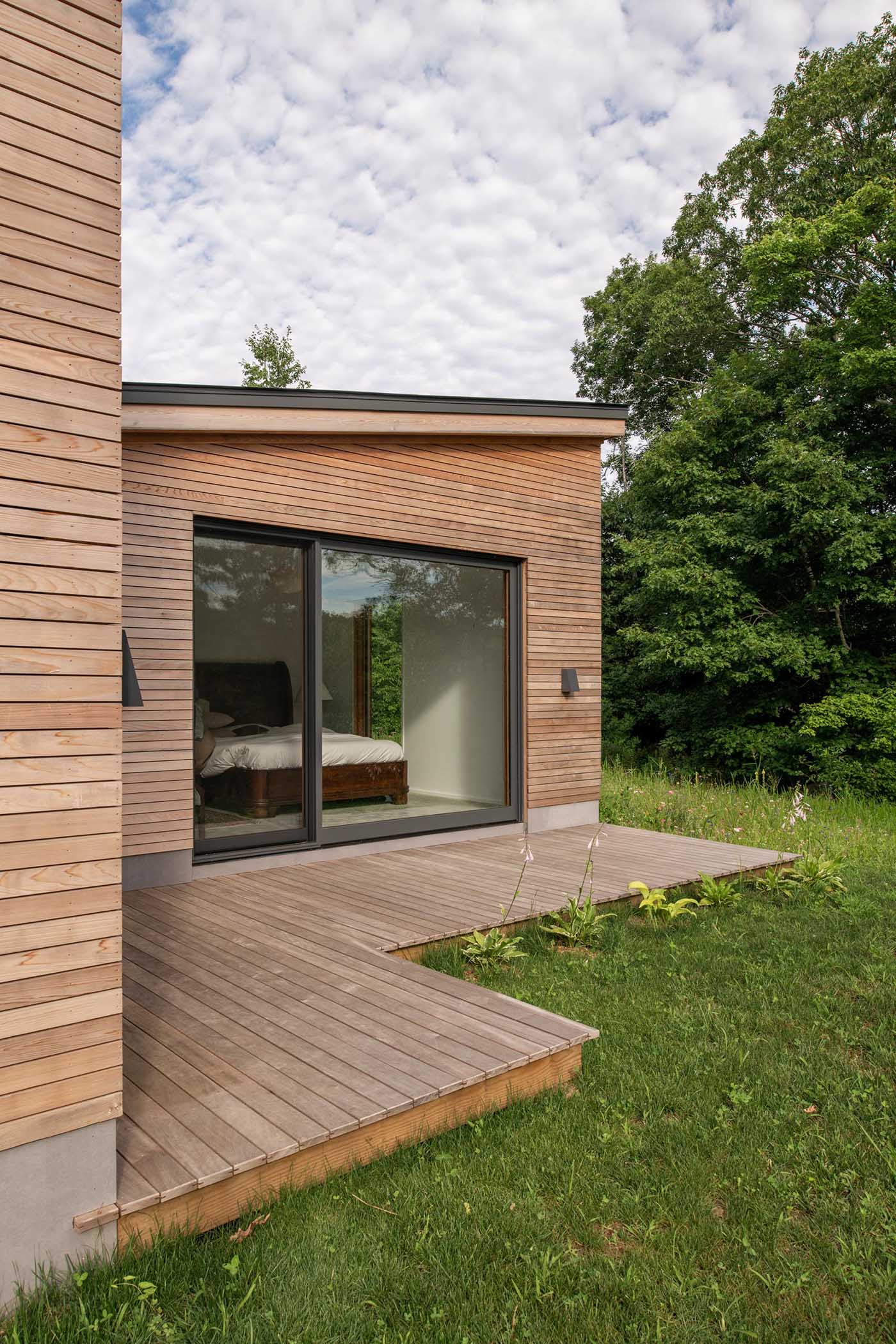 A deck wraps around this modern home, while the charcoal-colored window frames provide a contrast to the wood and complement the metal roof and garage door.