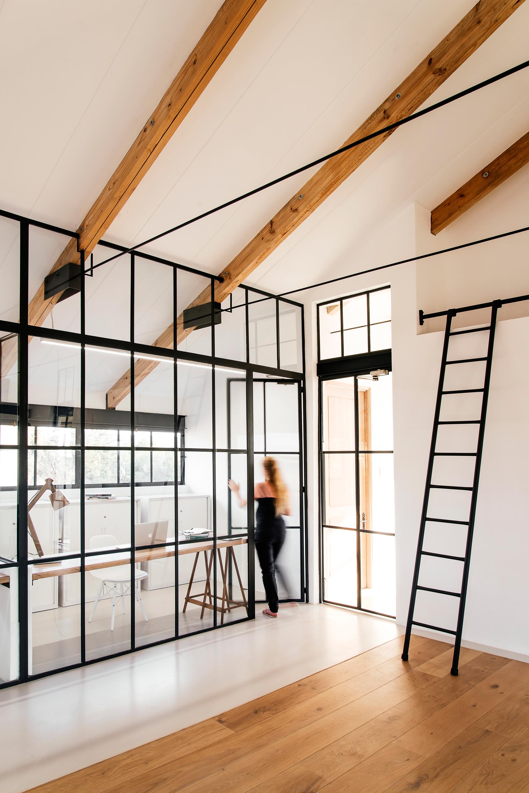 A home office is enclosed behind a glass wall, with a door that blends into its surroundings.