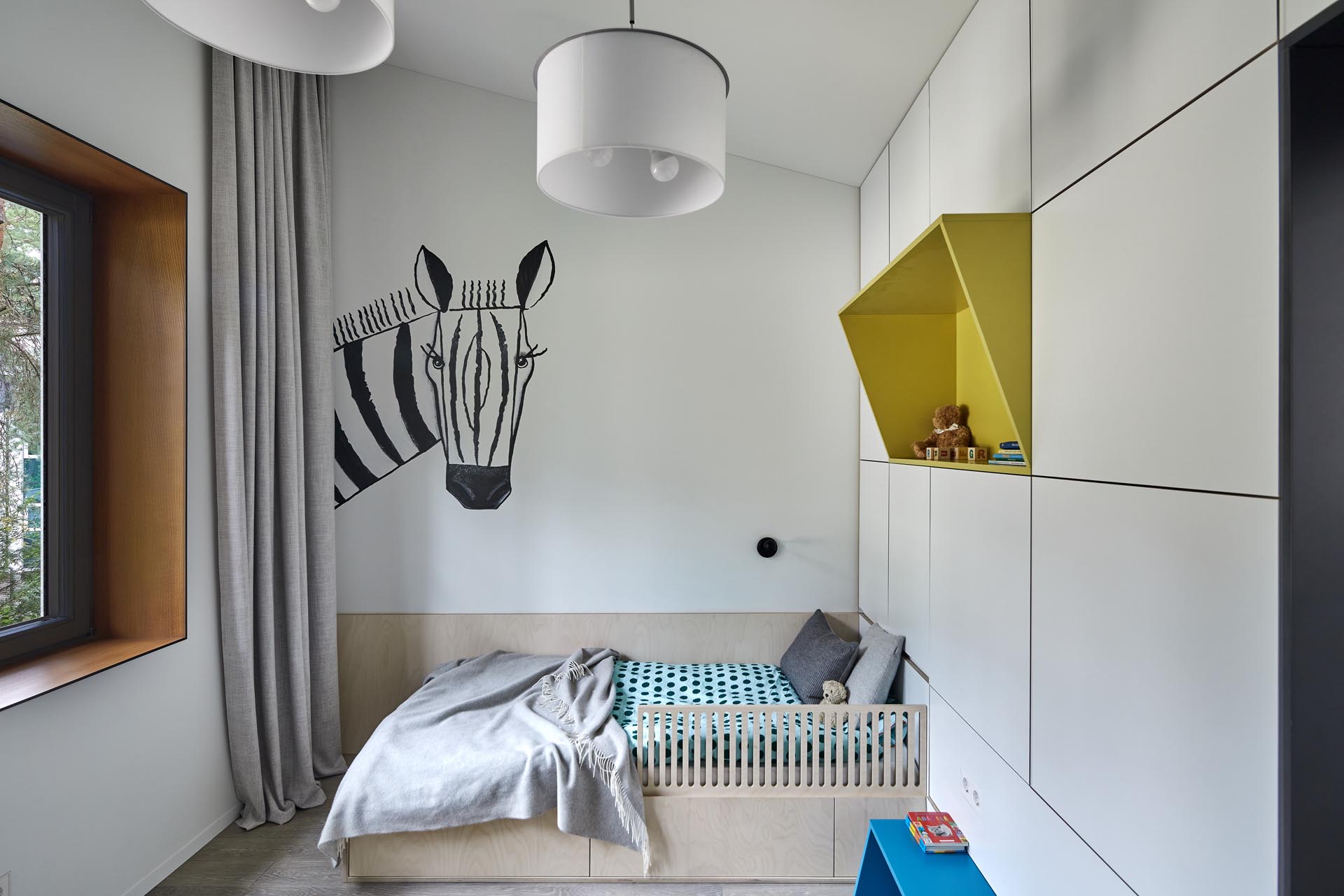 In this modern kid's bedroom, there's a zebra art feature, as well as a colorful yellow shelf and a green desk surrounded by storage.