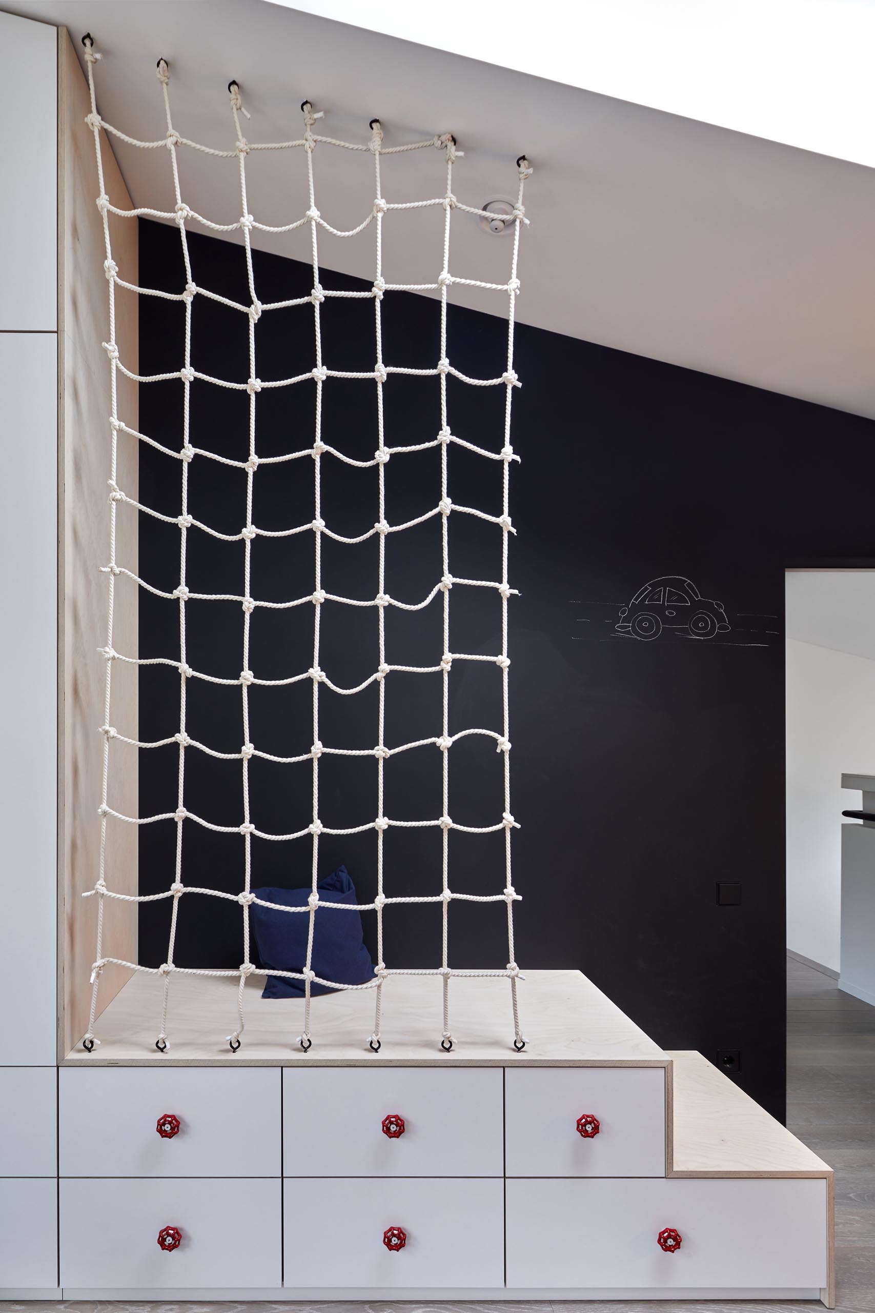 In this modern kid's bedroom, there's a chalkboard wall, built-in stepped storage, and a net accent.