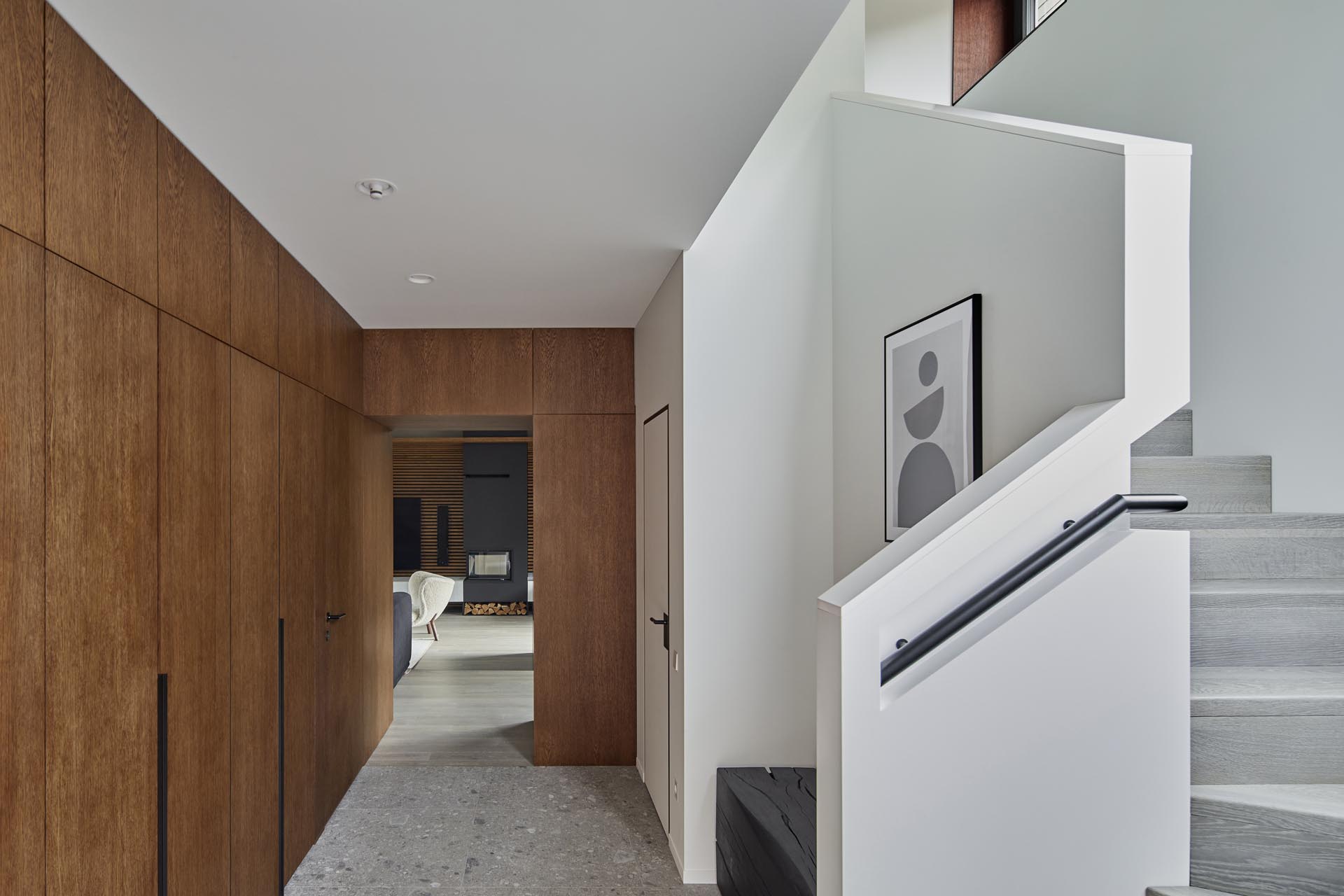 This modern entryway includes wood cabinets and a burnt wood bench. Stairs with a built-in handrail lead to the upstairs.