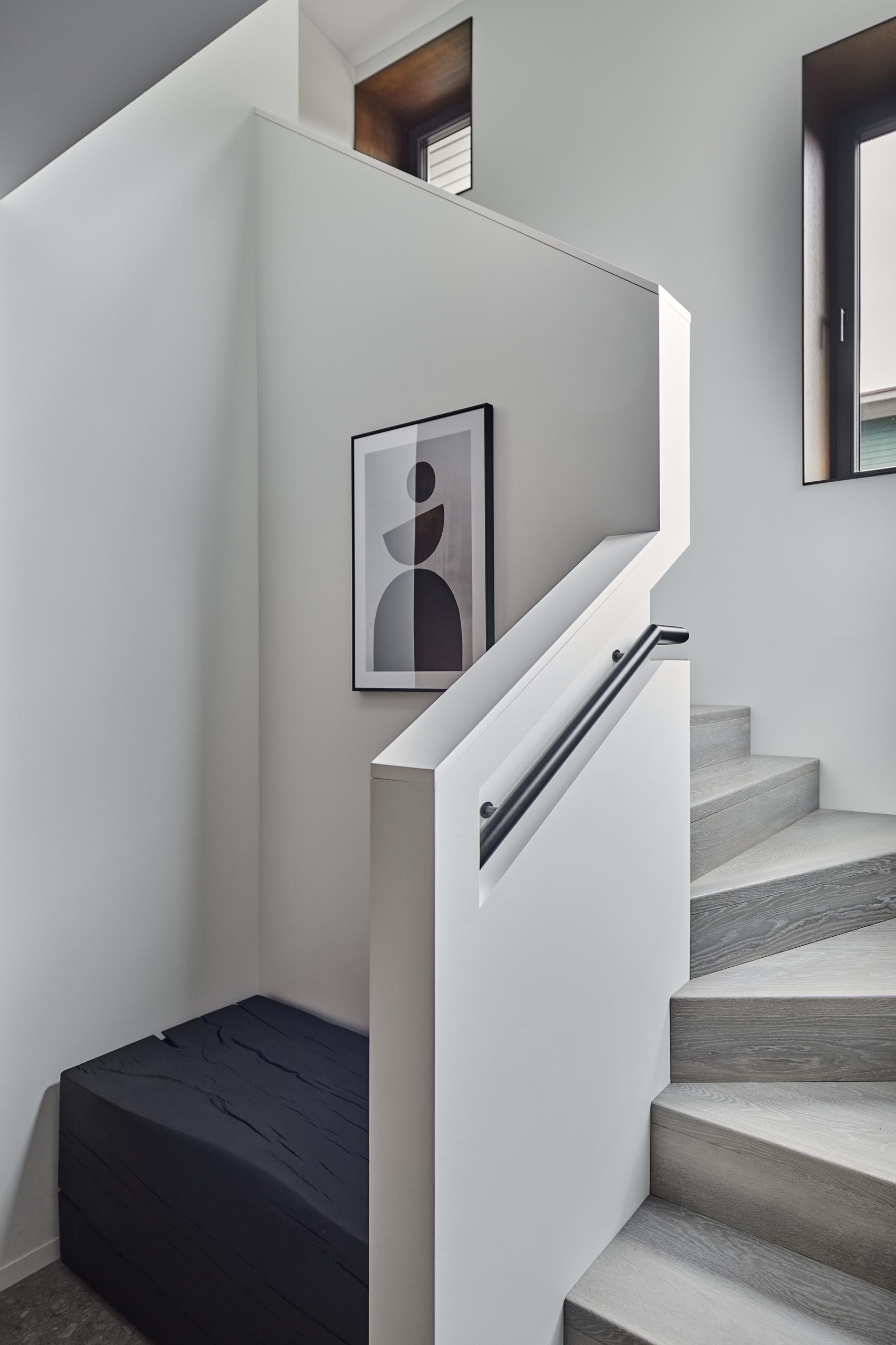 This modern entryway includes wood cabinets and a burnt wood bench. Stairs with a built-in handrail lead to the upstairs.