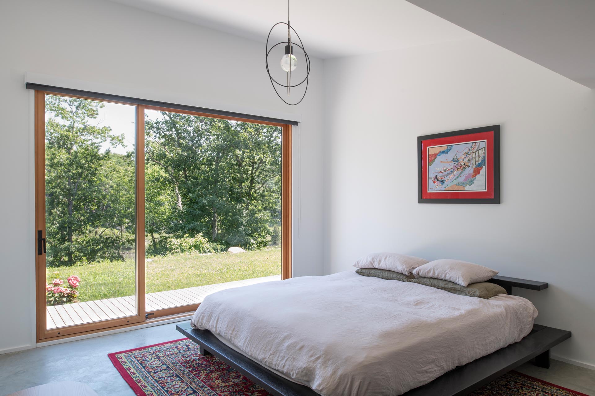 A minimalist bedroom with white walls, modern furniture, and a large window that looks out onto the marshland.