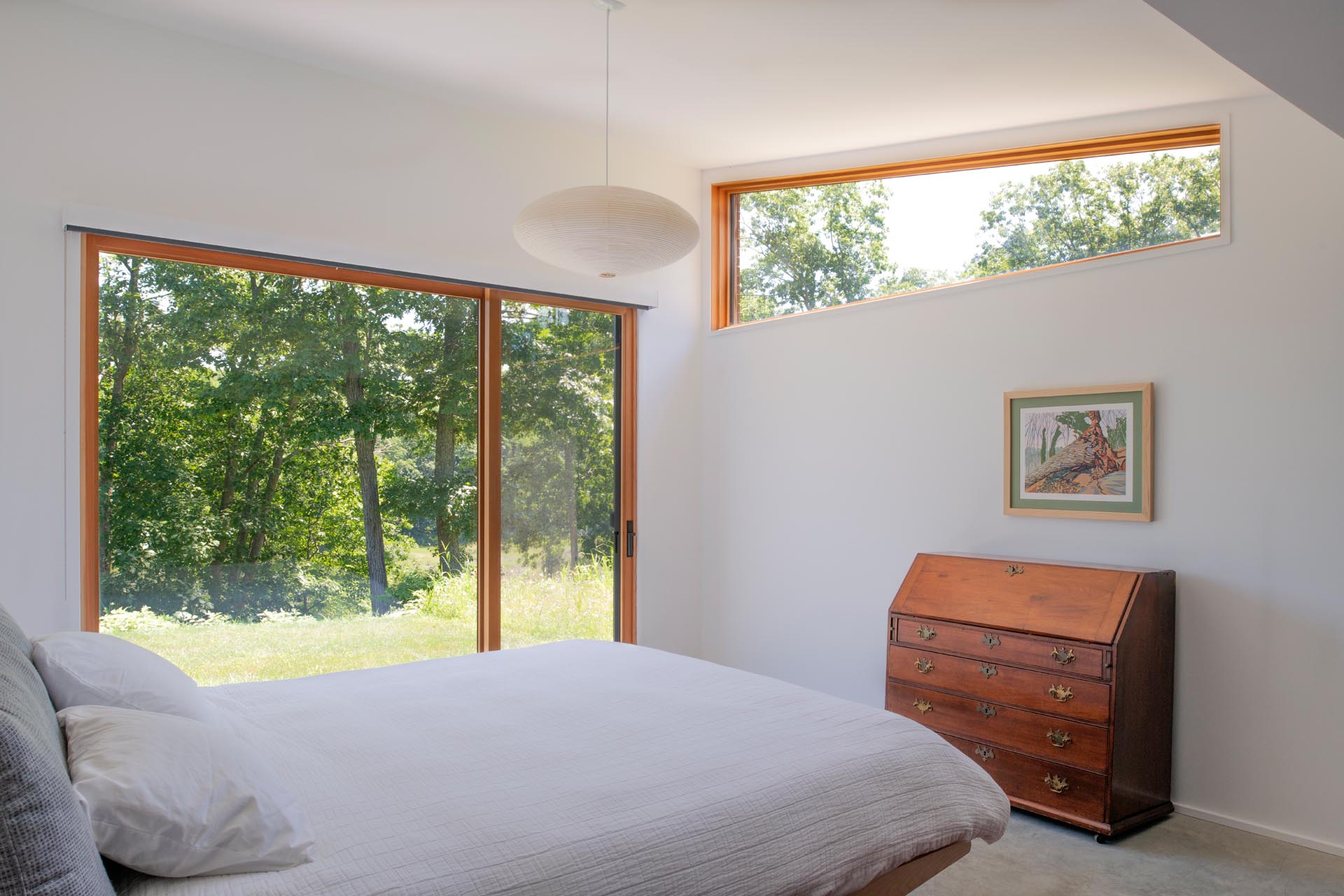 A simple bedroom with white walls, minimal furniture, and a large window that looks out onto the marshland.